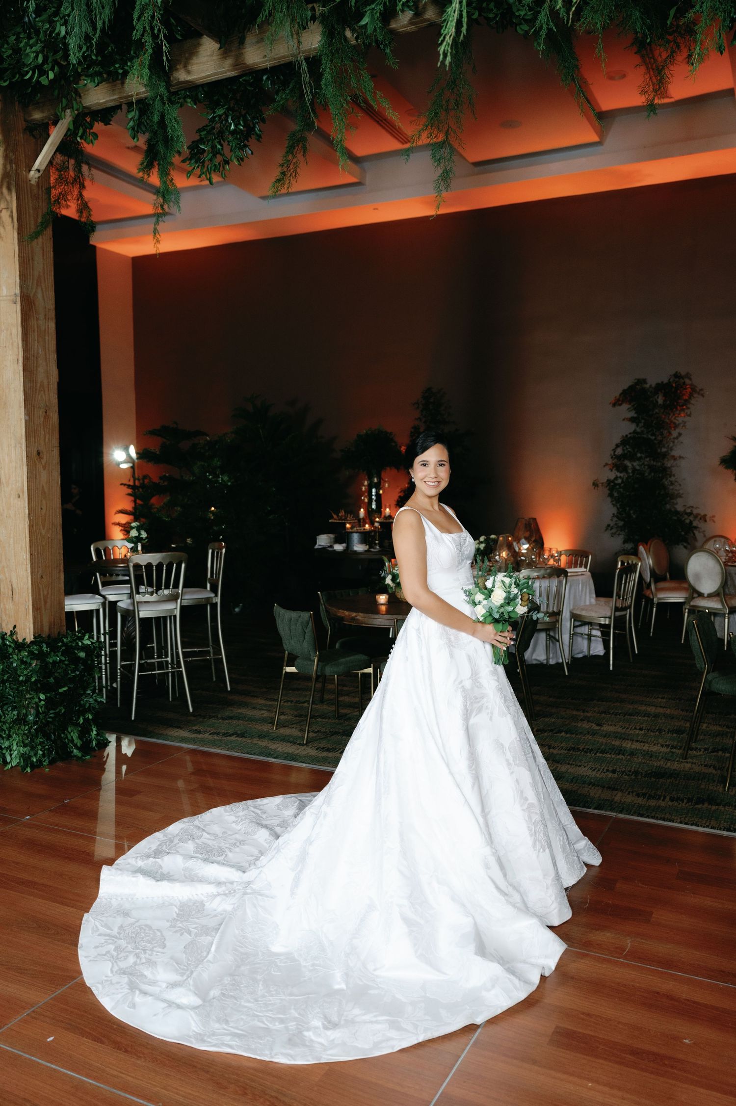 A stunning white wedding gown with intricate lace details and long train on hardwood floor in an elegant reception venue.
