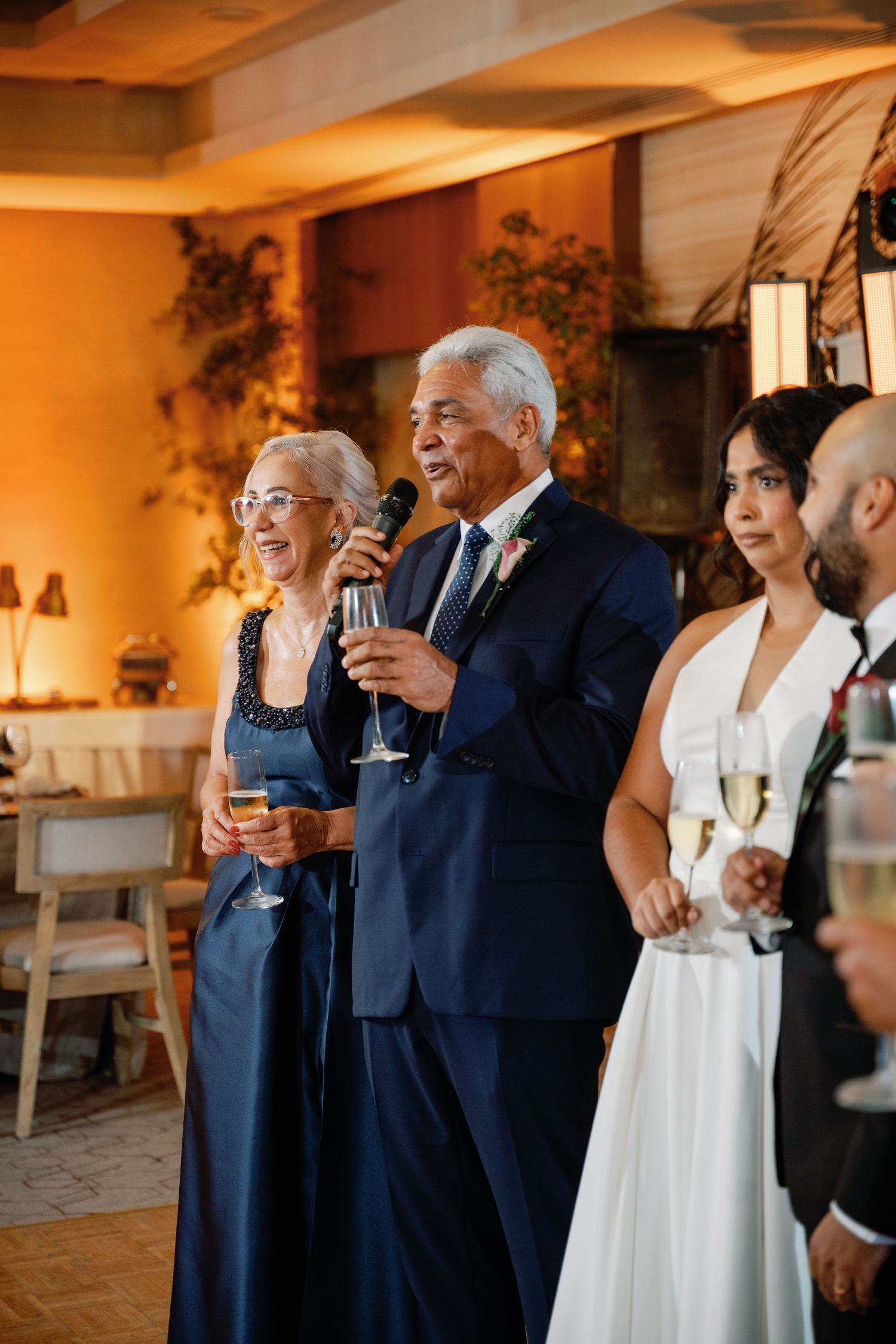 Wedding guests in formal attire gathered indoors for celebratory toasts during a reception.