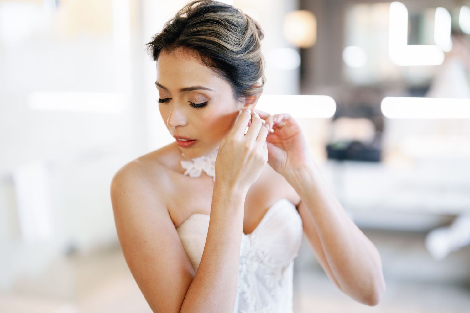 A bride in a white lace gown puts on her earring while getting ready on her wedding day.
