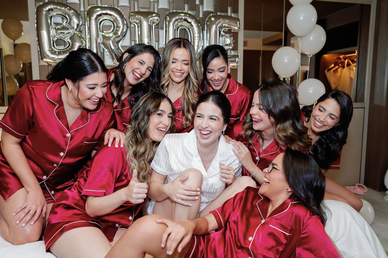 Wedding party in matching red satin robes laughs together during pre-ceremony preparations.