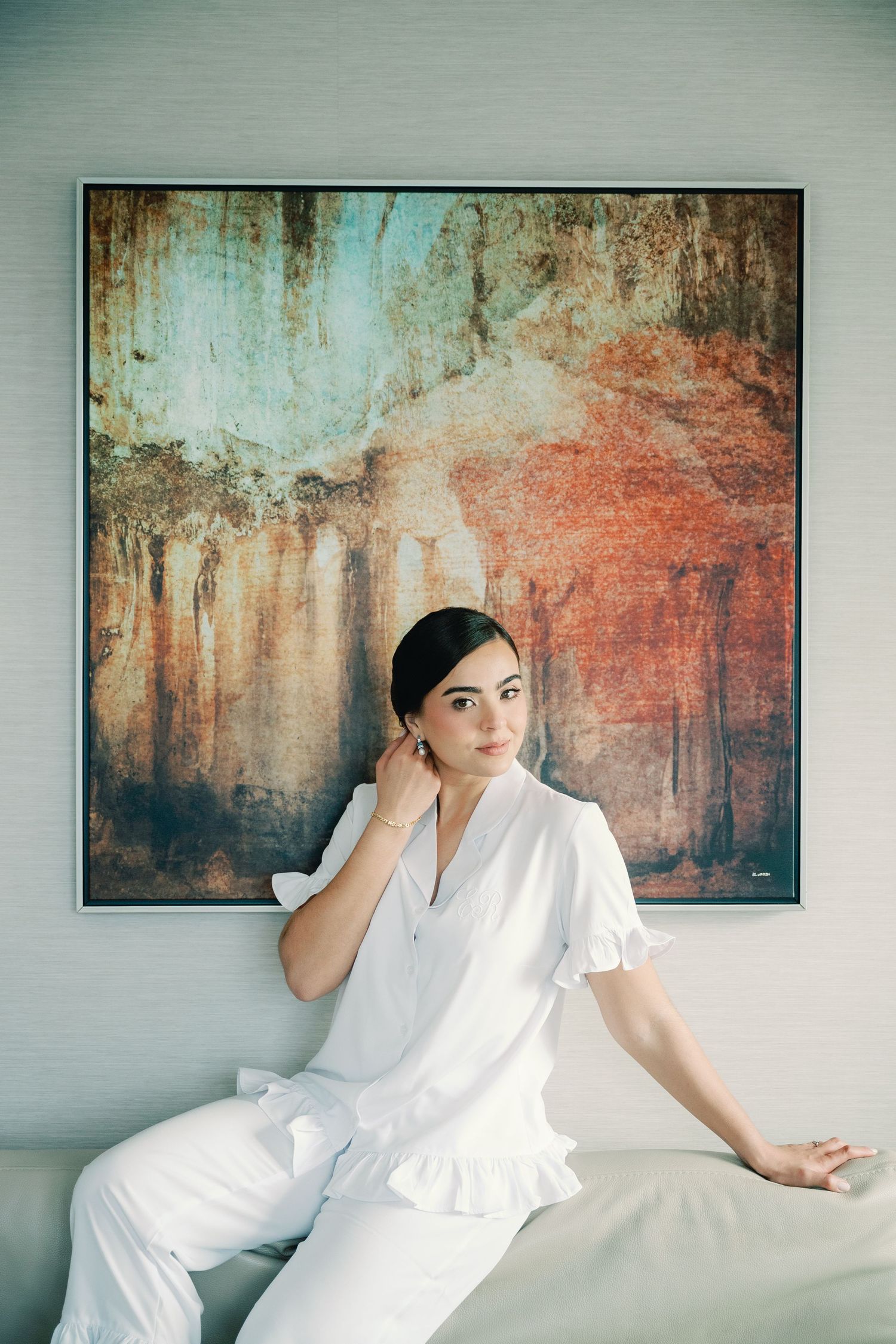 A person in white clothing reclines on a couch beneath abstract wall art with warm orange and gray tones.