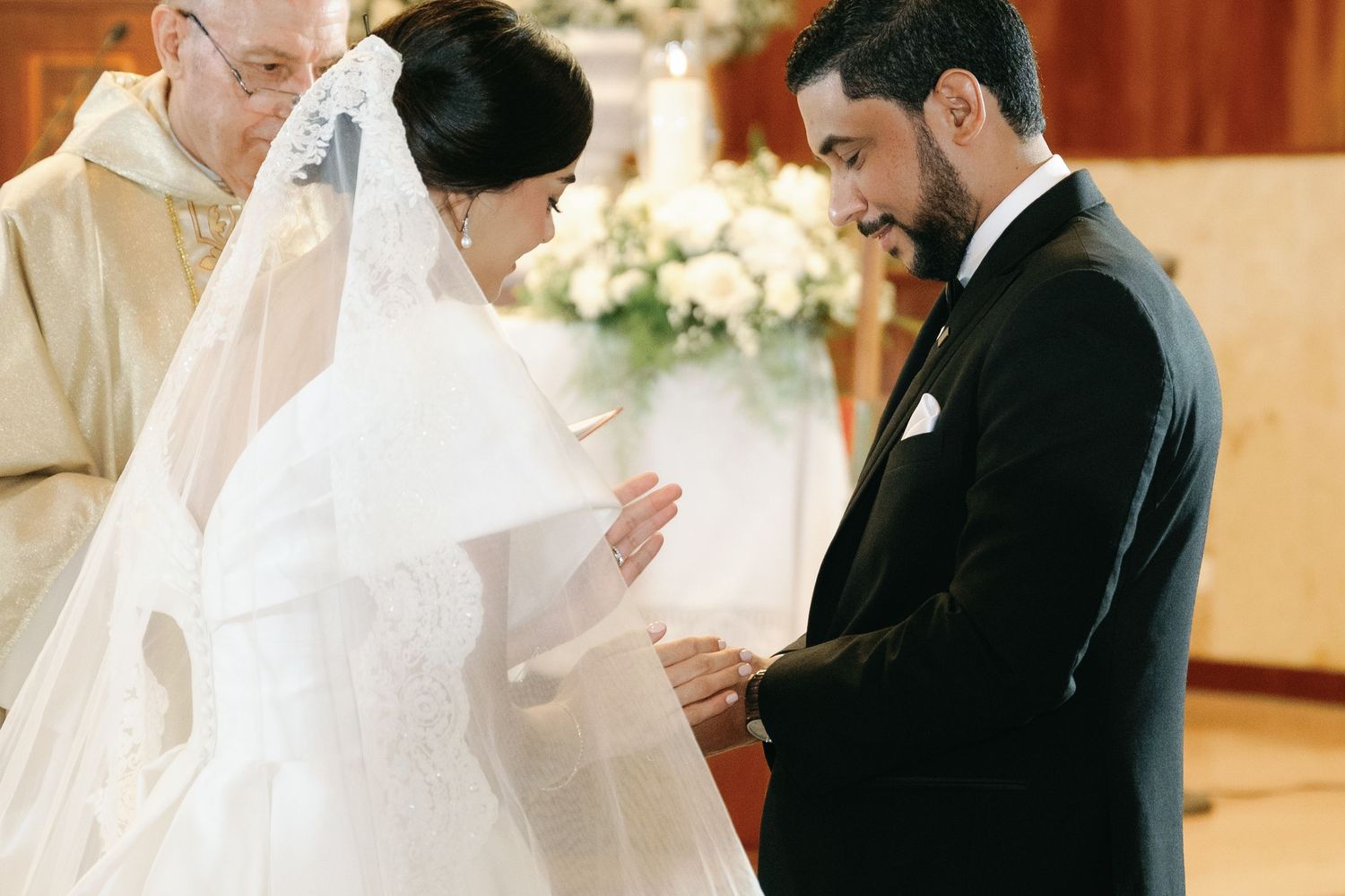 A couple exchanges rings during a traditional wedding ceremony in a church with white floral decorations.