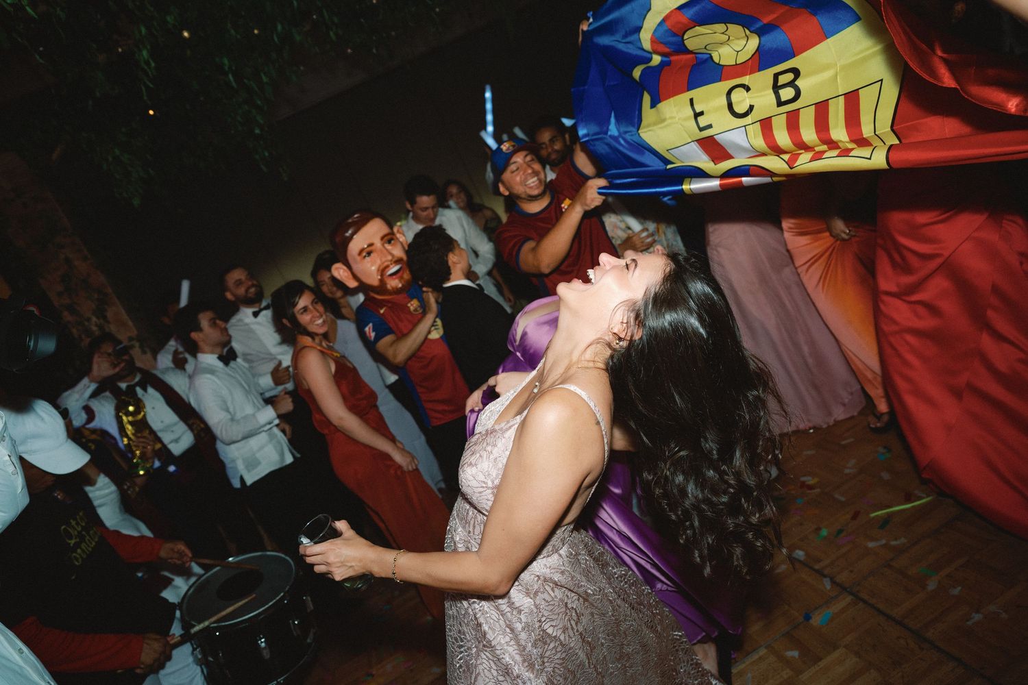 People dancing and celebrating at a lively party with colorful decorations visible in the background.