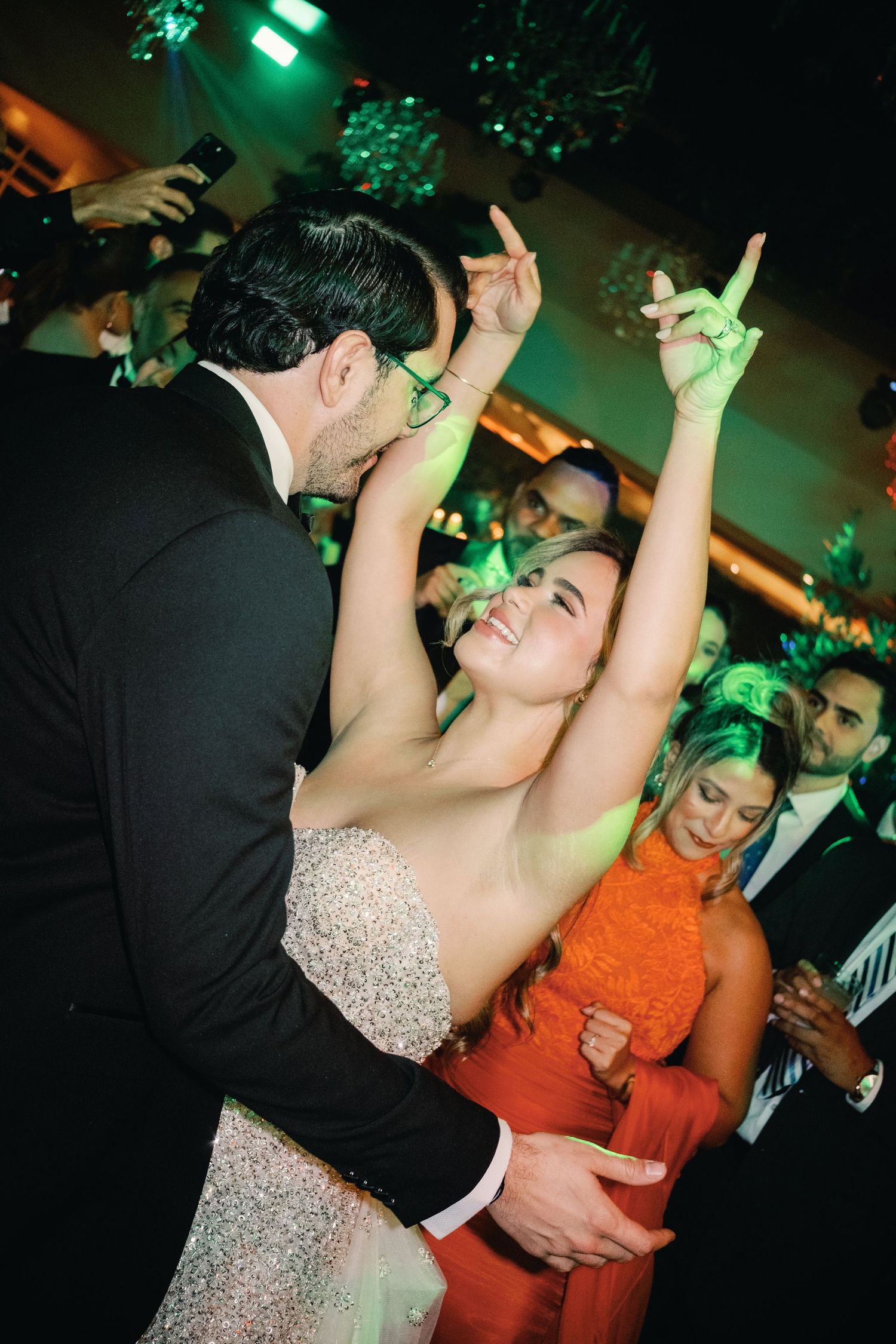 Couples dancing at a wedding reception under green lighting while wearing formal attire.