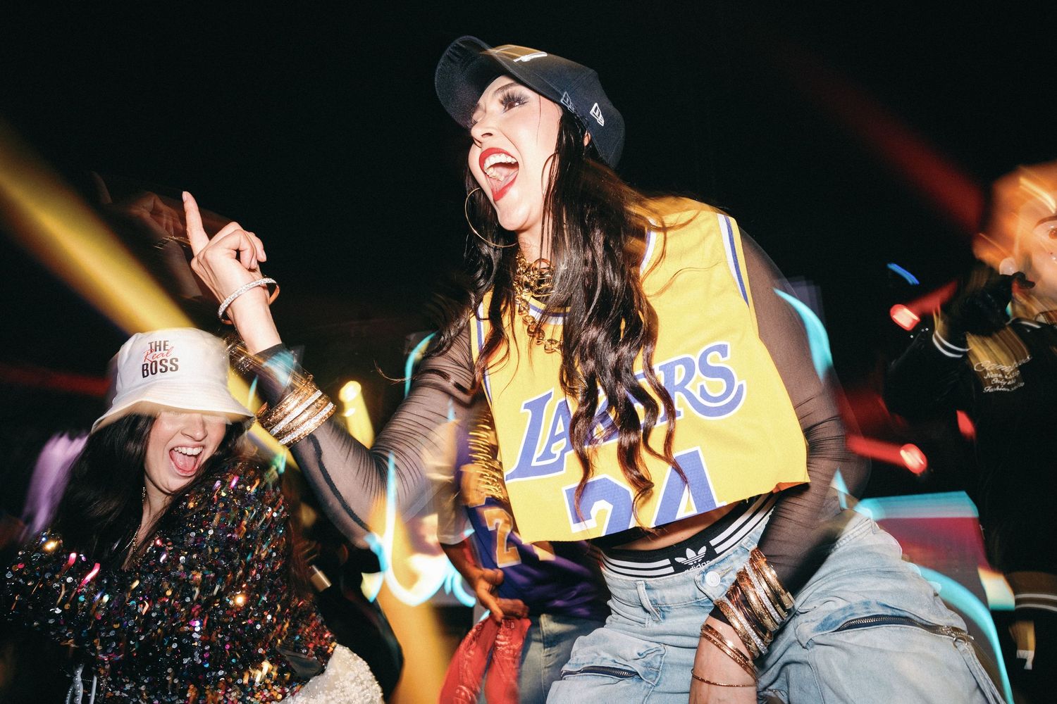 Energetic concert scene with performers on stage in dynamic poses with colorful lighting and crowd energy.