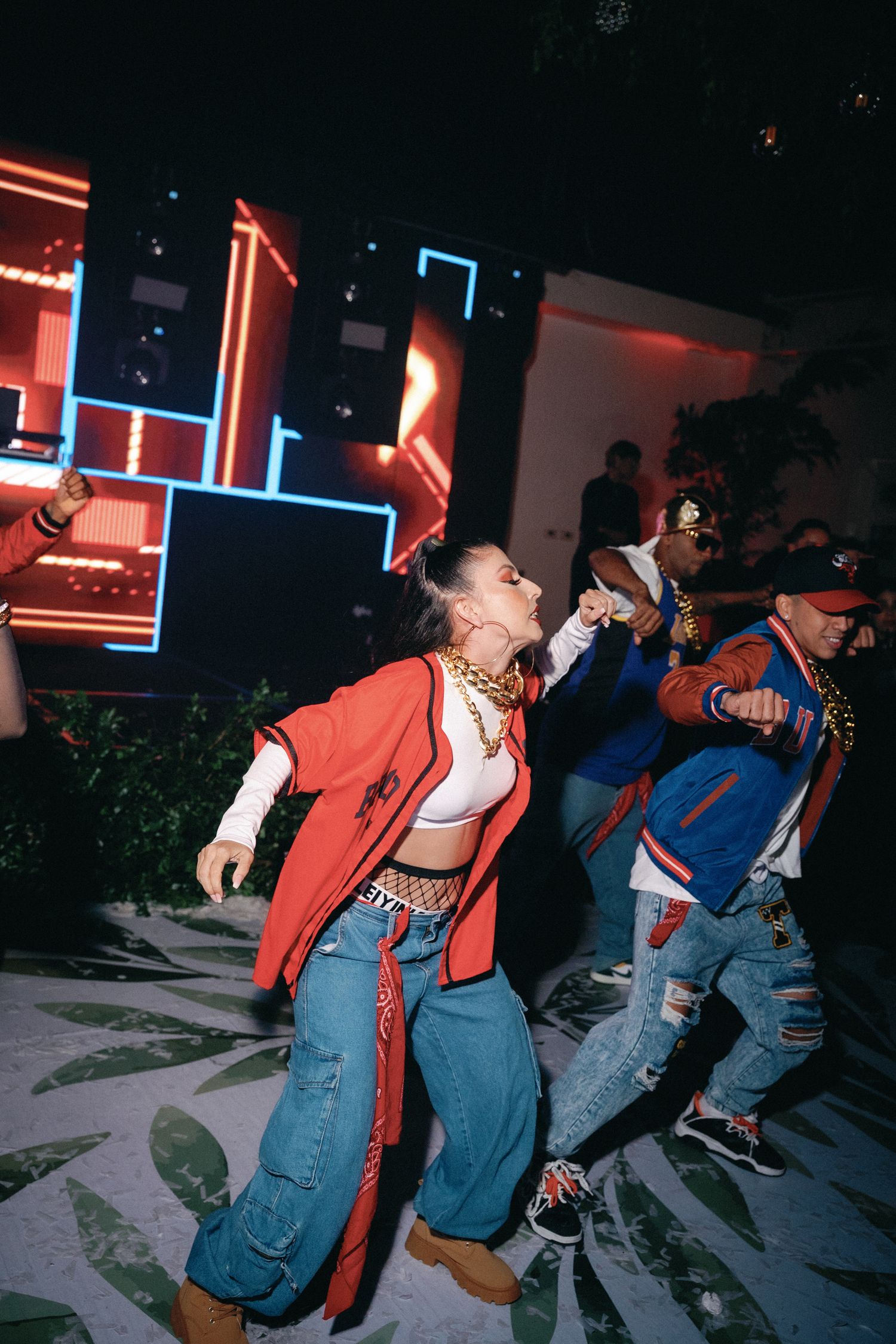 Group of dancers in denim overalls and red jackets performing a synchronized dance routine.