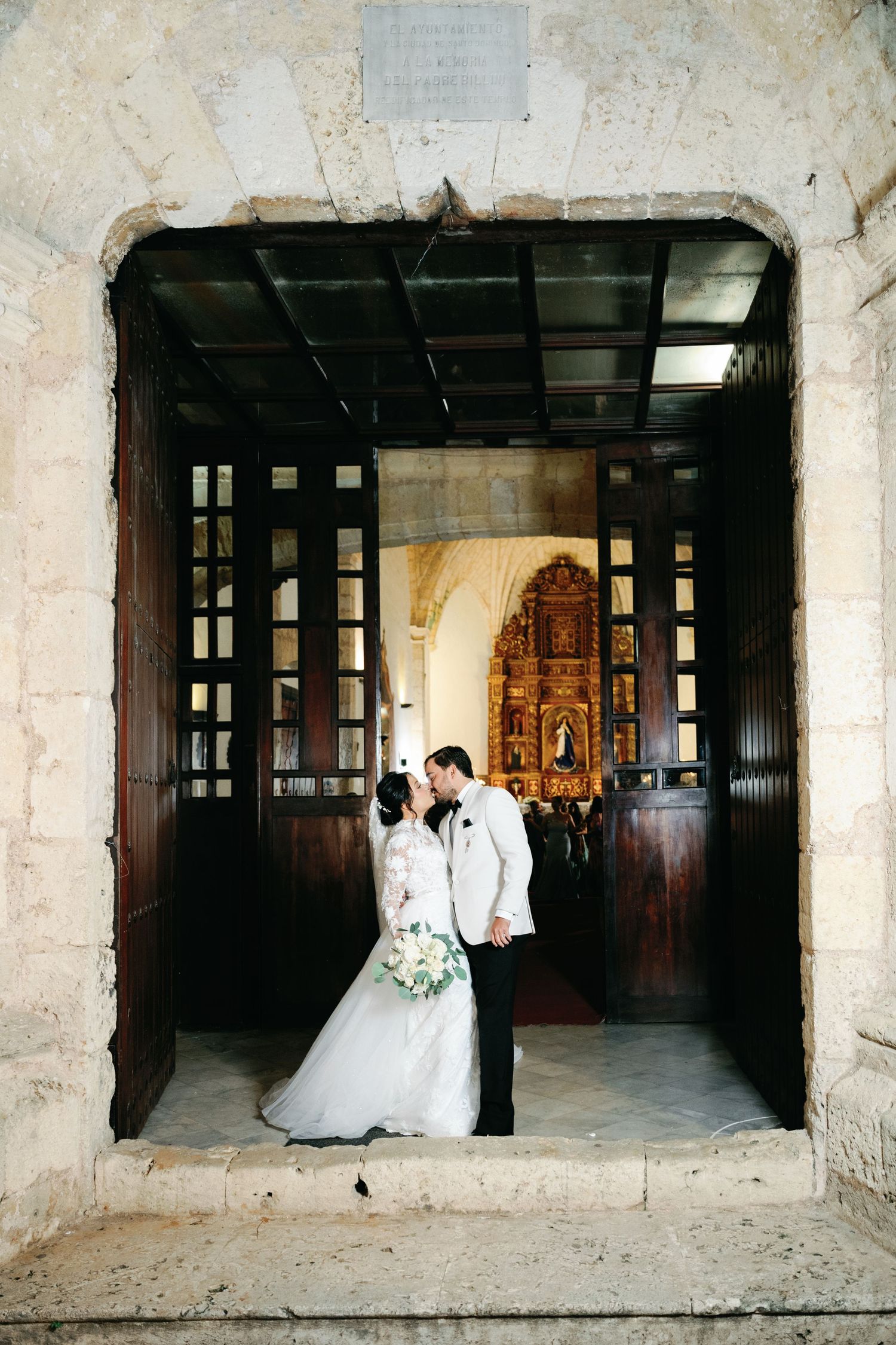 A wedding couple poses in a rustic stone hallway with dramatic lighting and architectural elements.