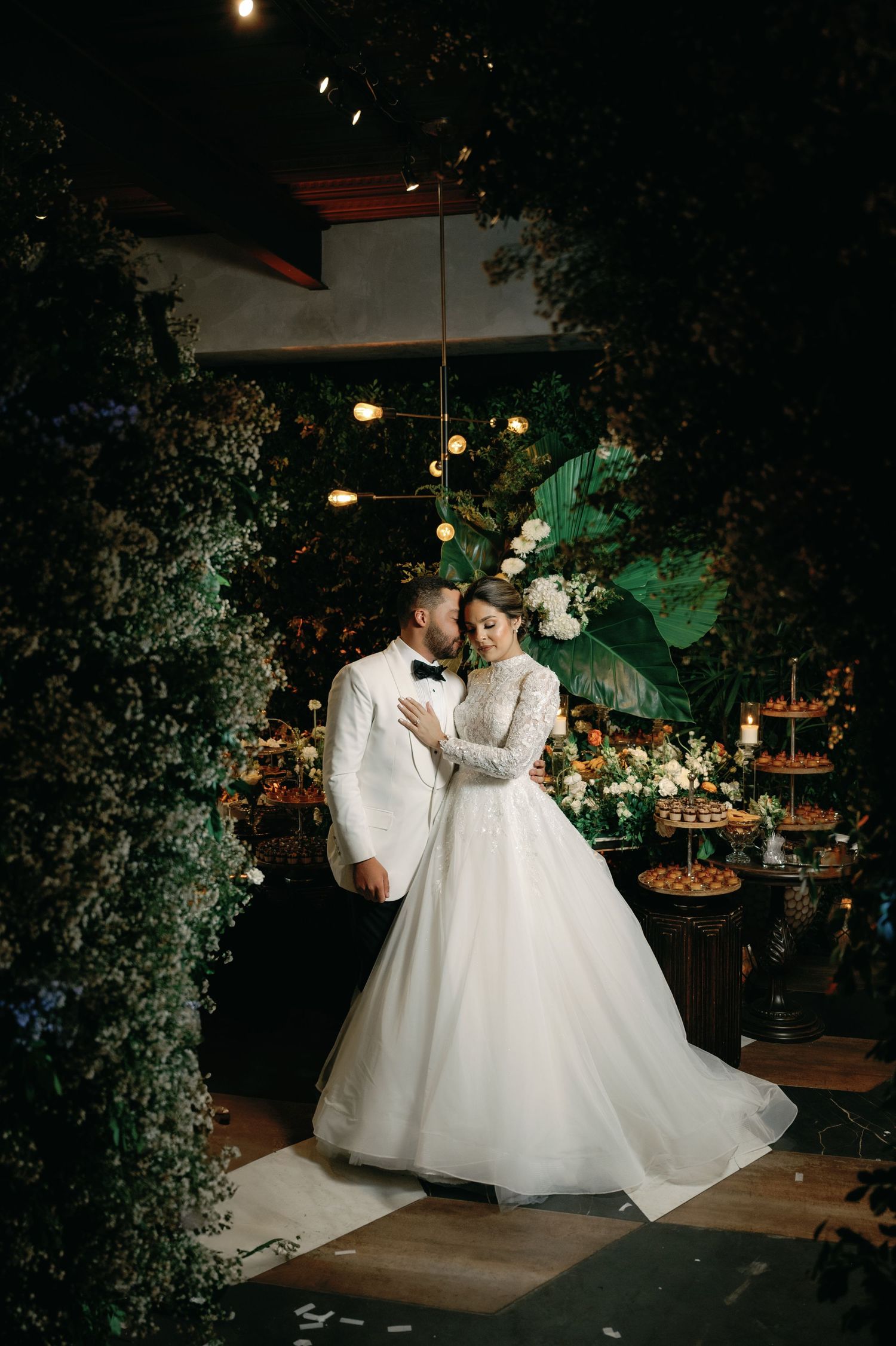 Romantic wedding couple dancing together in an elegant venue with lush greenery and ambient lighting creating a magical atmosphere.