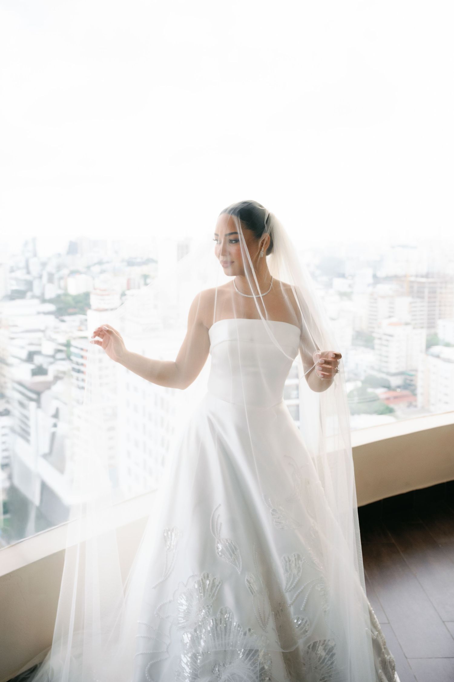 A bride in a flowing white wedding gown stands by a window in a sequence of graceful poses.