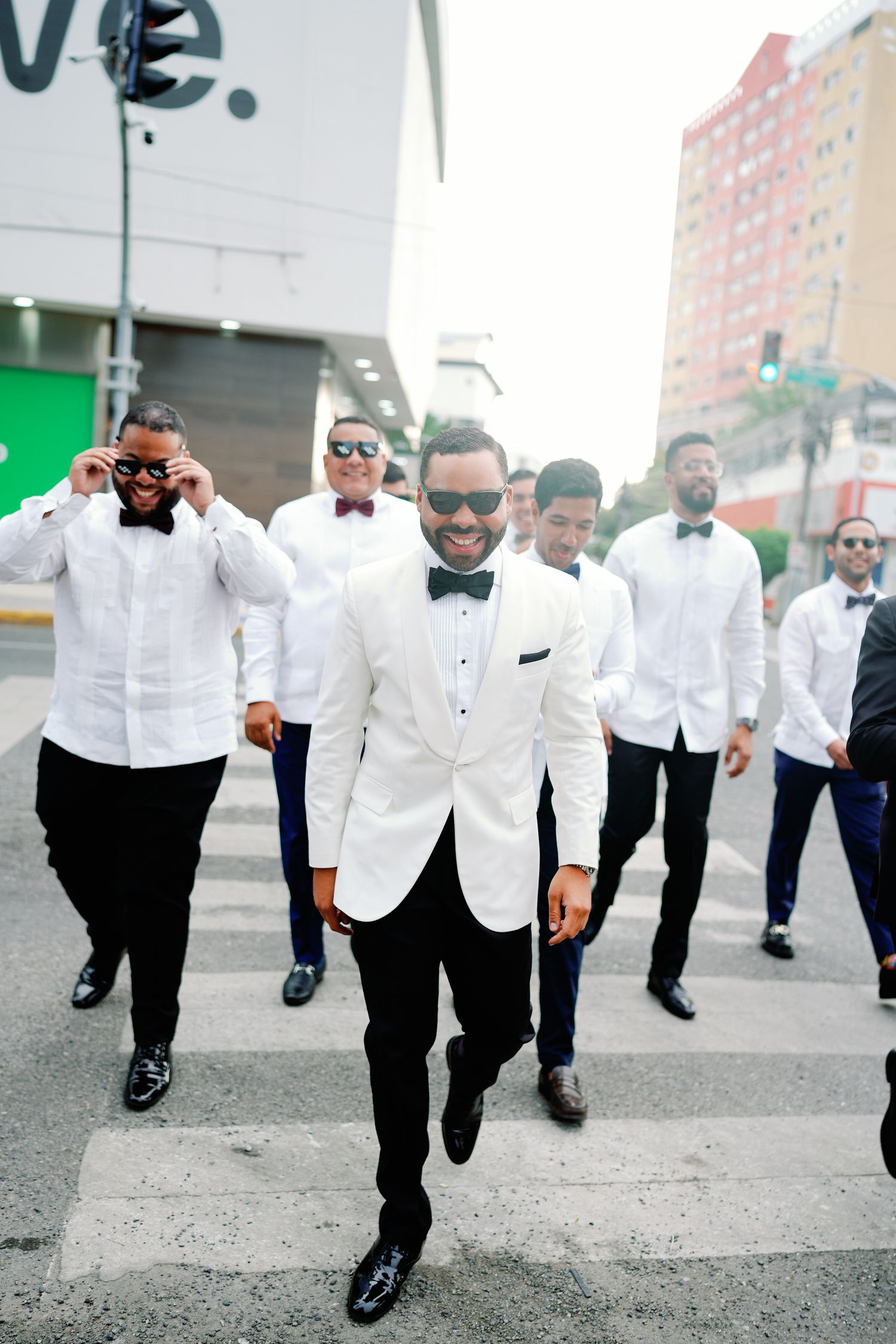 Groomsmen in matching white dinner jackets and black pants walk together in a casual outdoor setting.