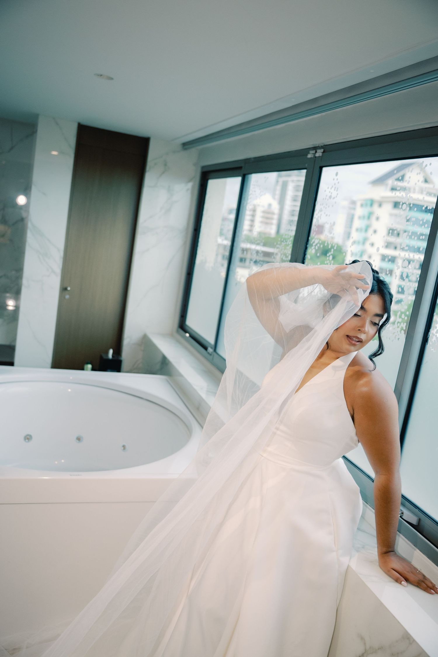 A flowing white wedding gown with a dramatic veil captured in a modern interior setting with natural lighting.