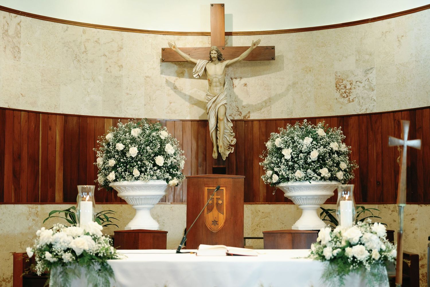 White floral arrangements and crosses decorate the interior of a traditional church sanctuary with wooden paneling.