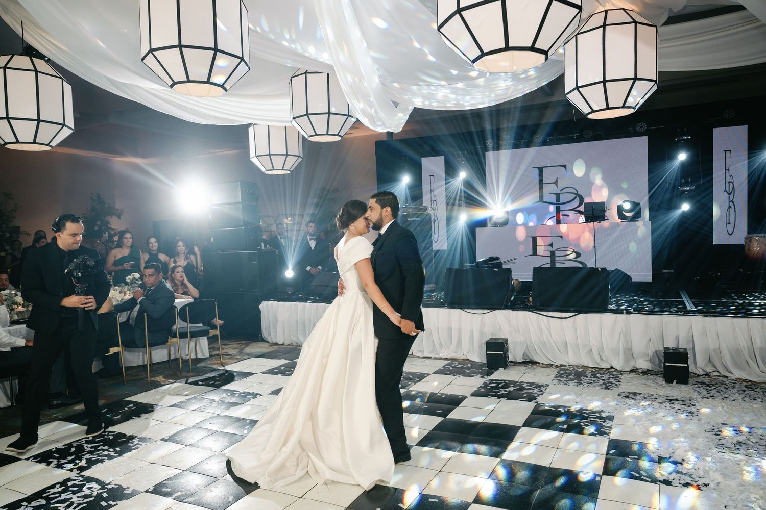 Wedding reception dance floor with hanging lantern lights and guests dancing in a dimly lit venue.
