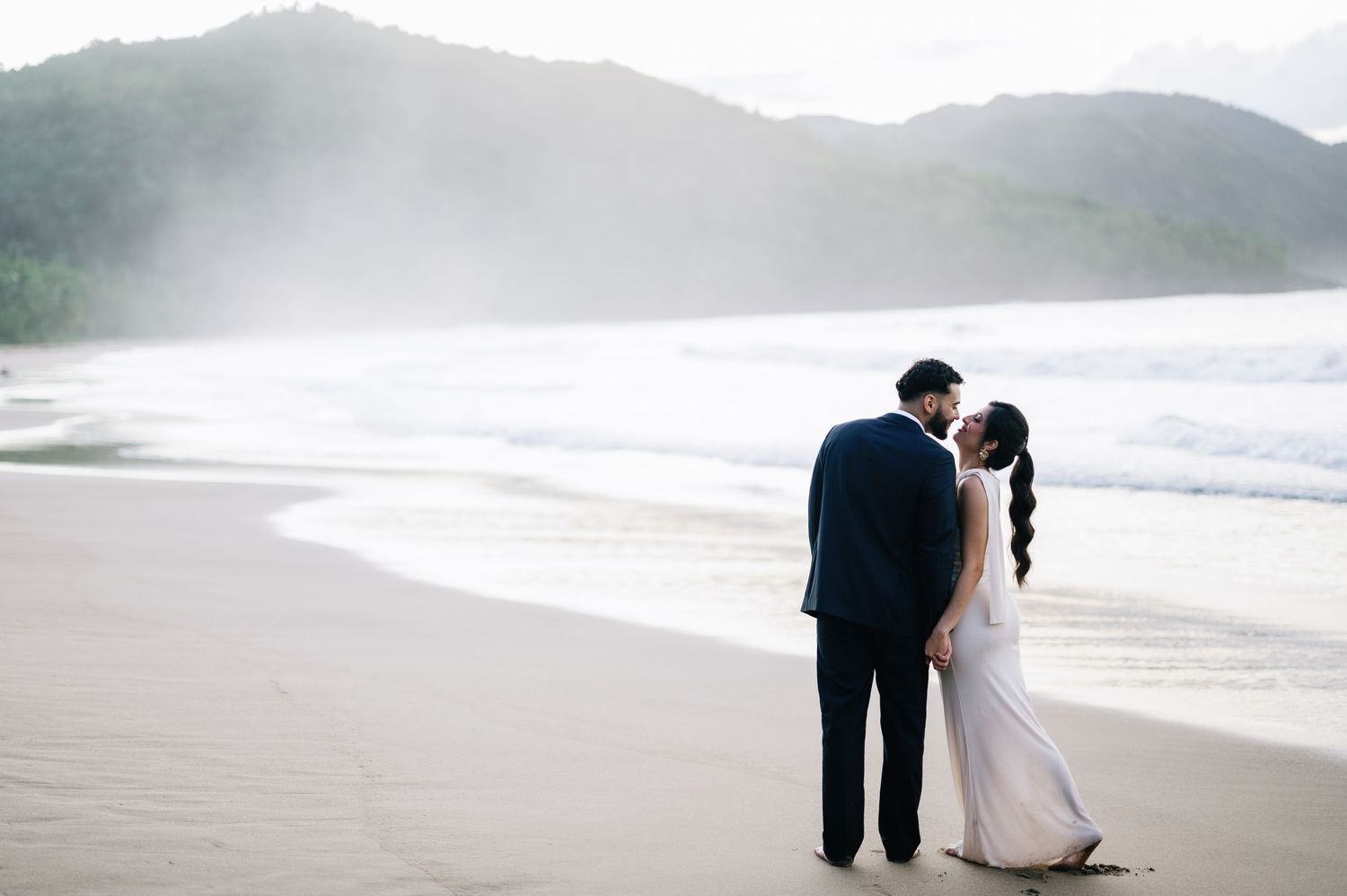 Silhouettes against a moody coastal landscape with mountains in the distance.