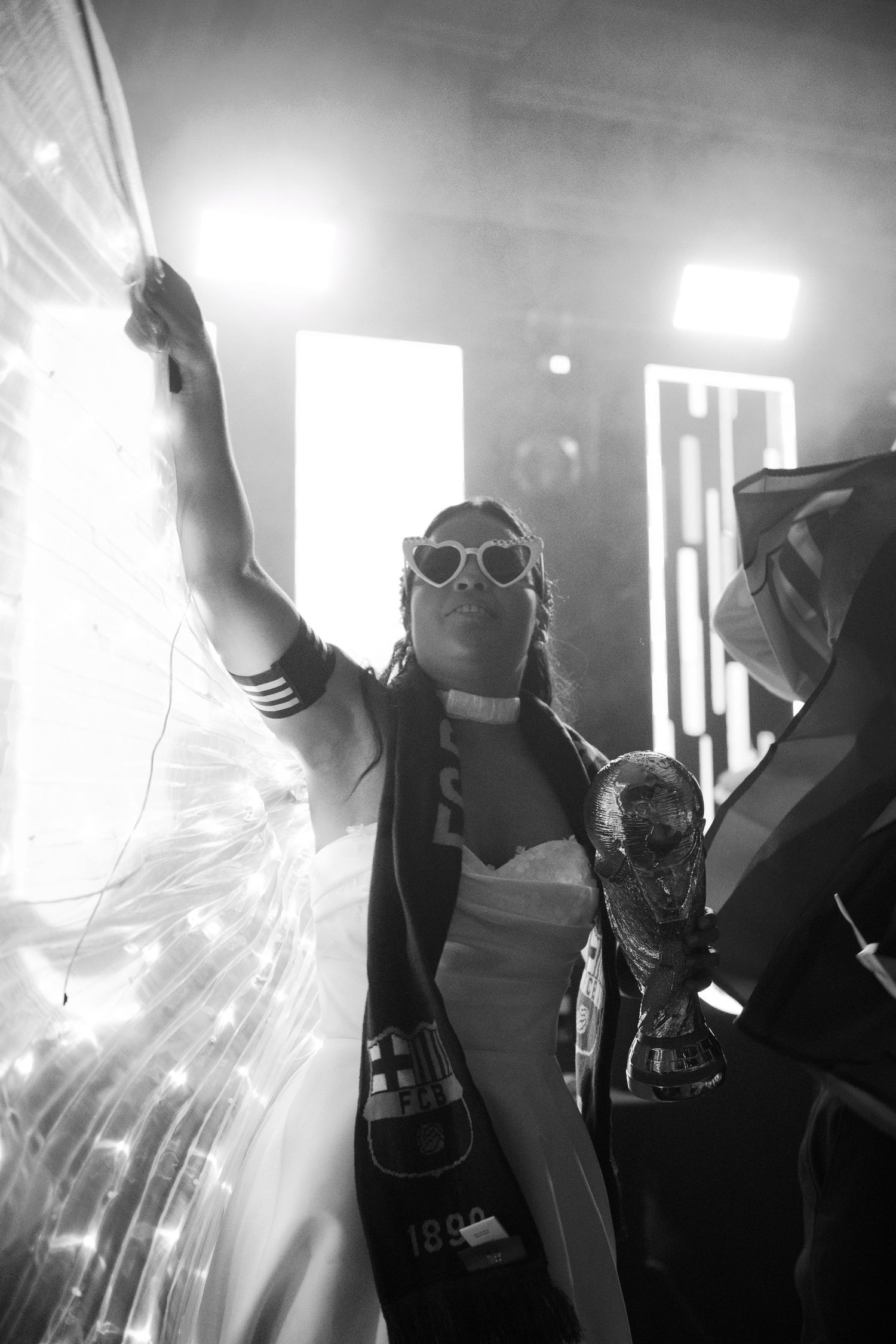 Party scene with bright stage lights and sunglasses-wearing figure raising arm in celebration.