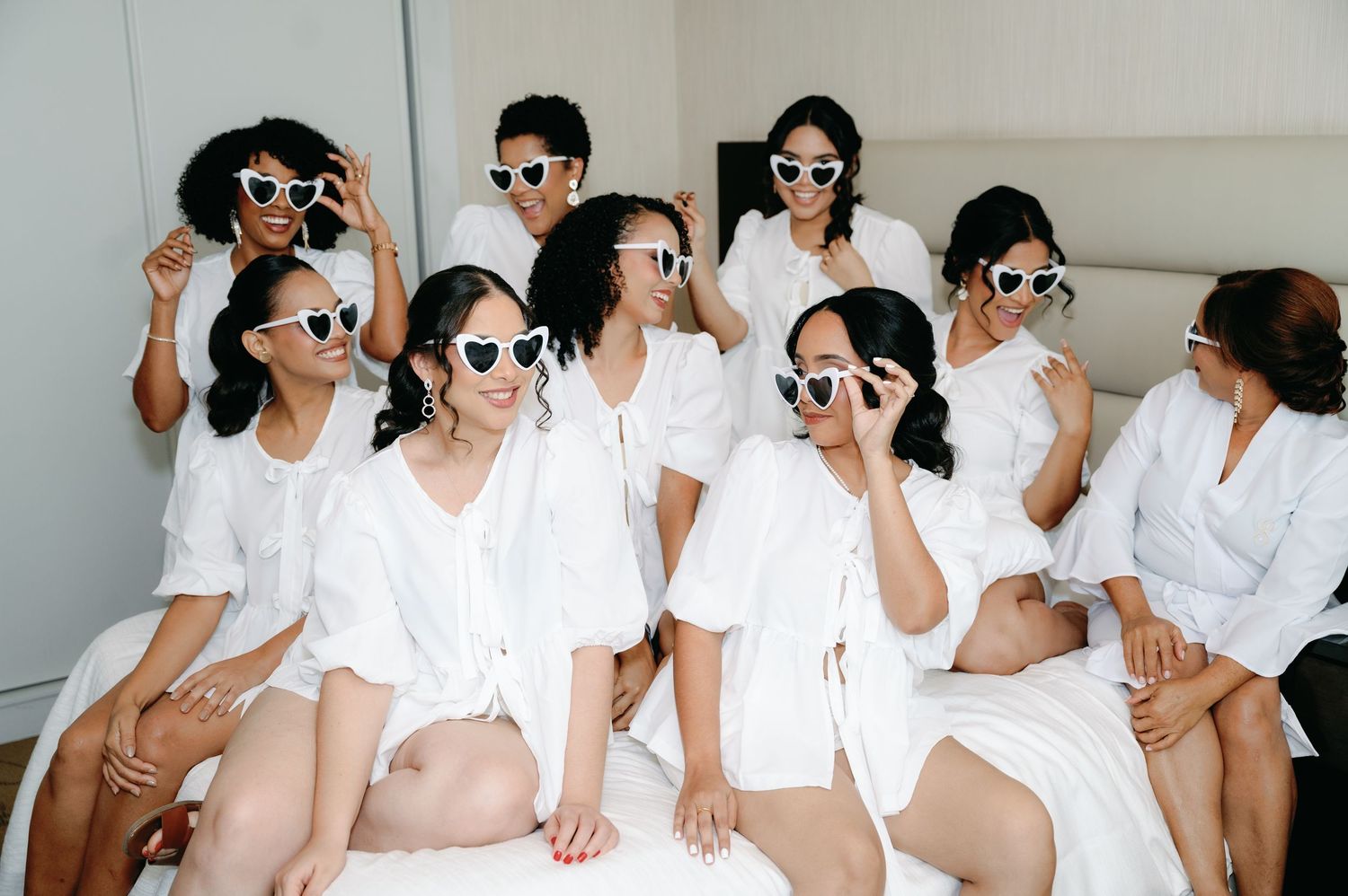 A group wearing matching white outfits and sunglasses pose together in a stylized fashion photo shoot.