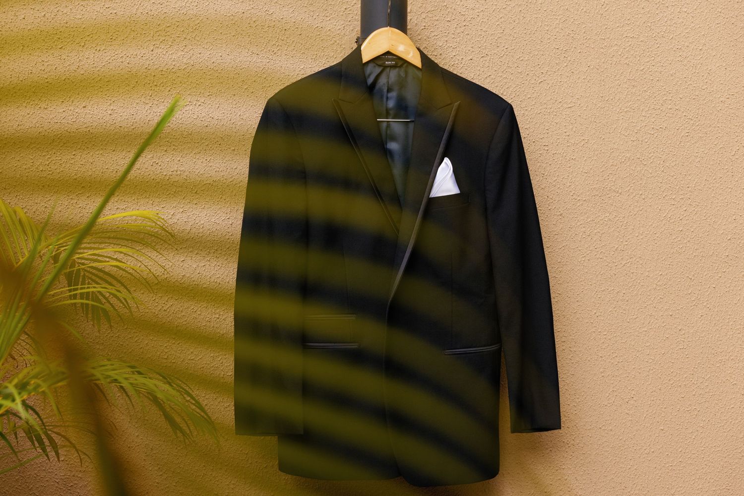 A black striped polo shirt displayed against a beige background with a subtle palm leaf shadow.