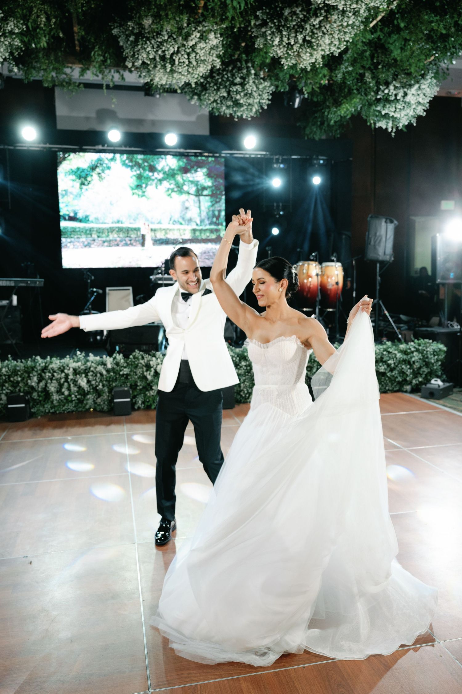 A couple performs an elegant dance sequence on an outdoor patio with dramatic lighting and greenery in the background.