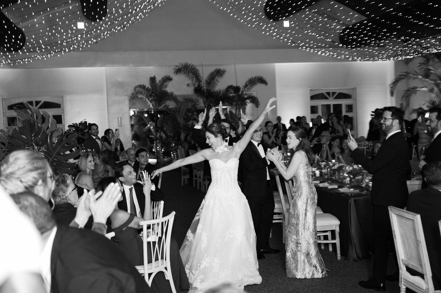 Black and white wedding reception dance floor scene with guests celebrating under twinkling lights.