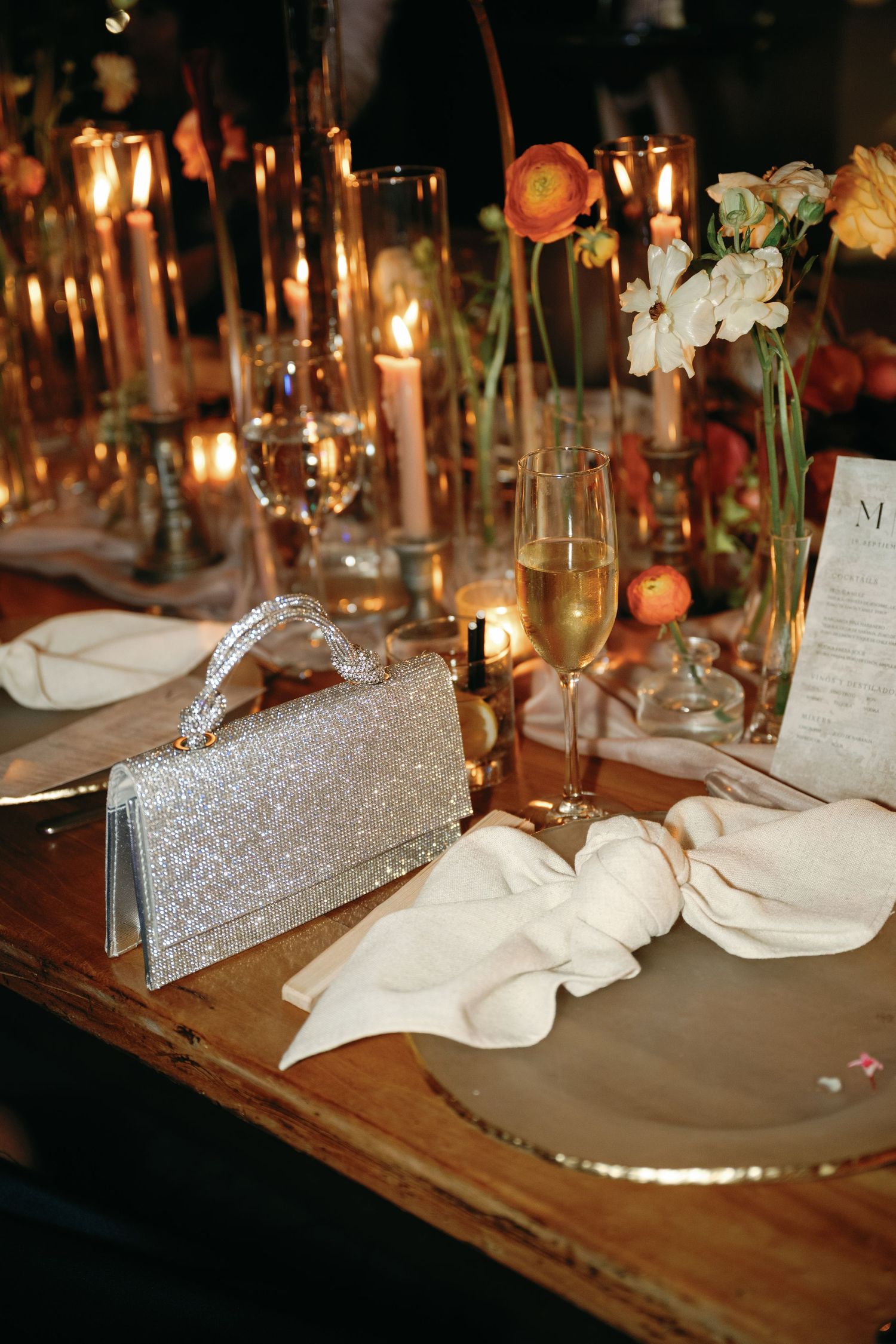 Elegant table setting with glittering silver clutch, white napkin, and candlelight creating romantic ambiance.