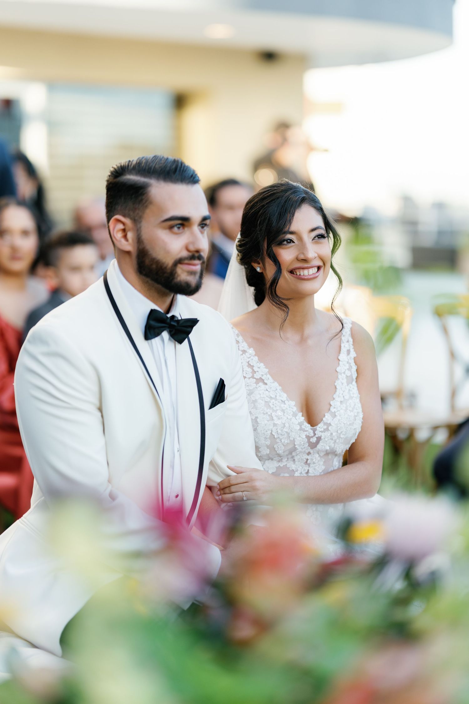 A couple in wedding attire shares an intimate moment at their reception, surrounded by soft floral decorations.