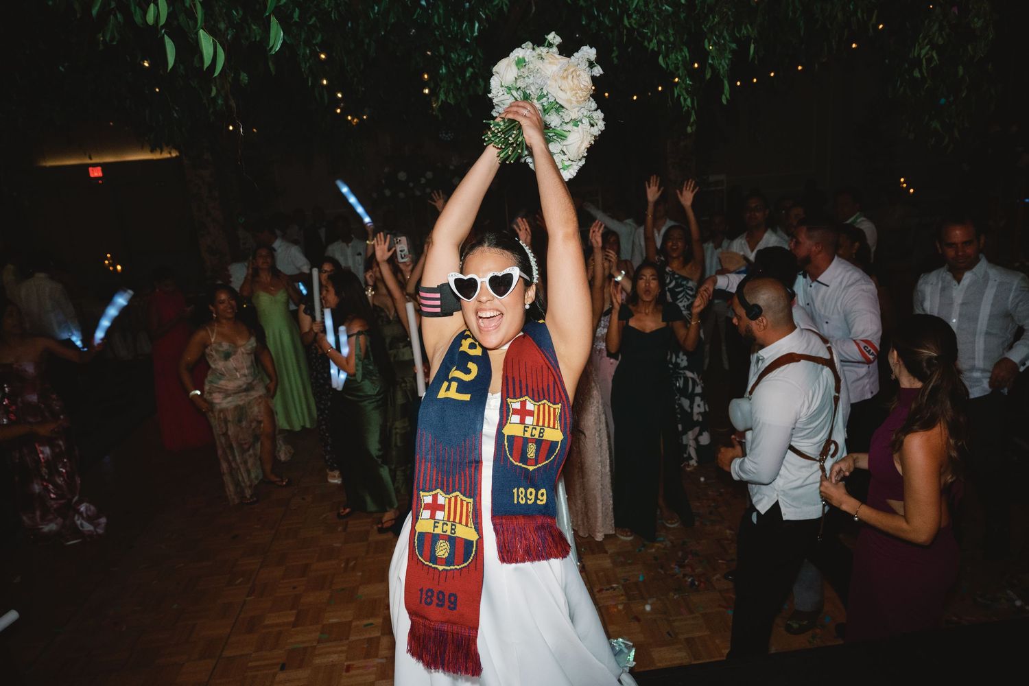 A group of people dancing and celebrating at a dimly lit party or reception venue.