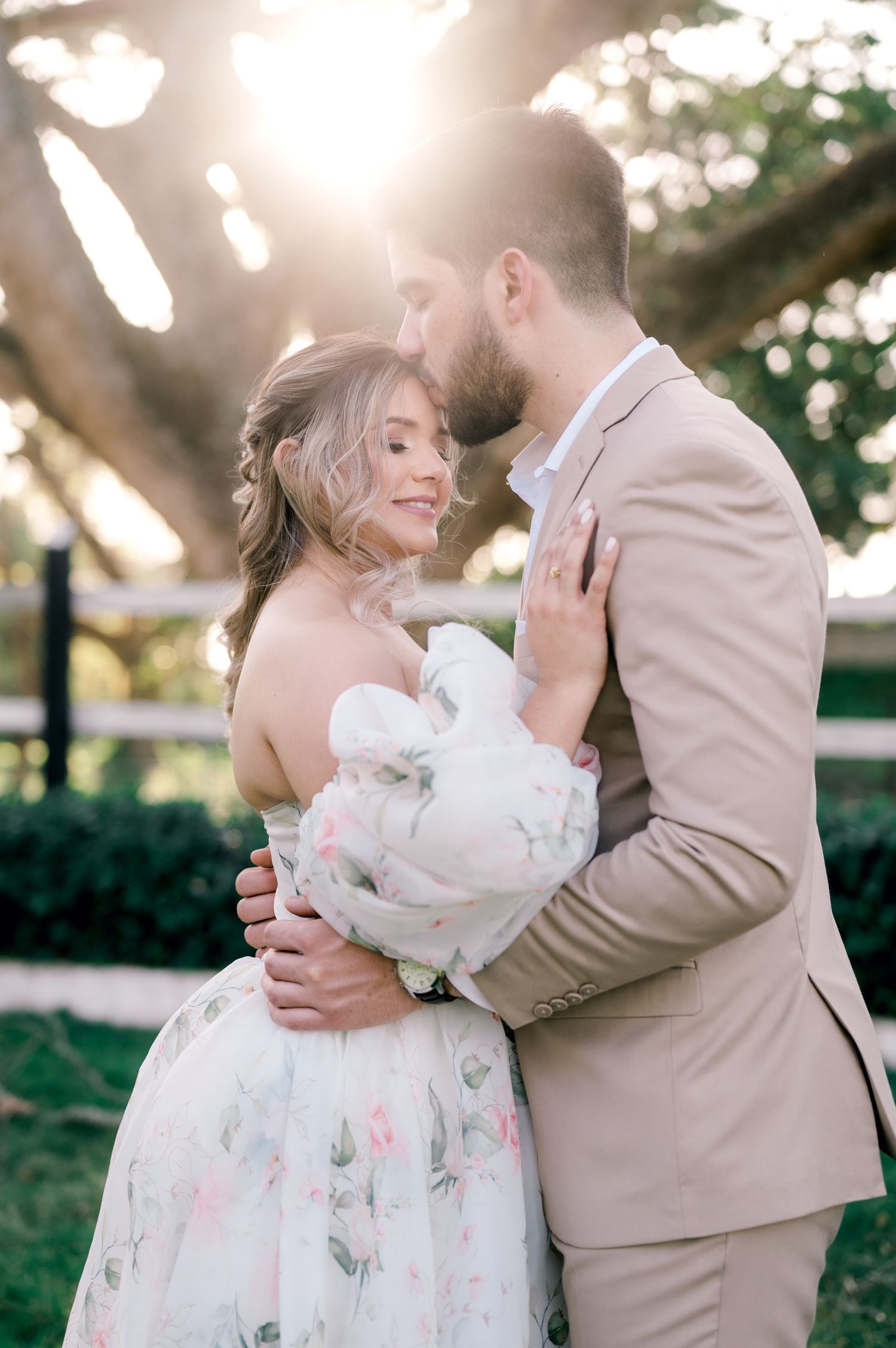 A romantic outdoor wedding scene shows a couple in beige and white embracing in a garden setting with natural sunlight.