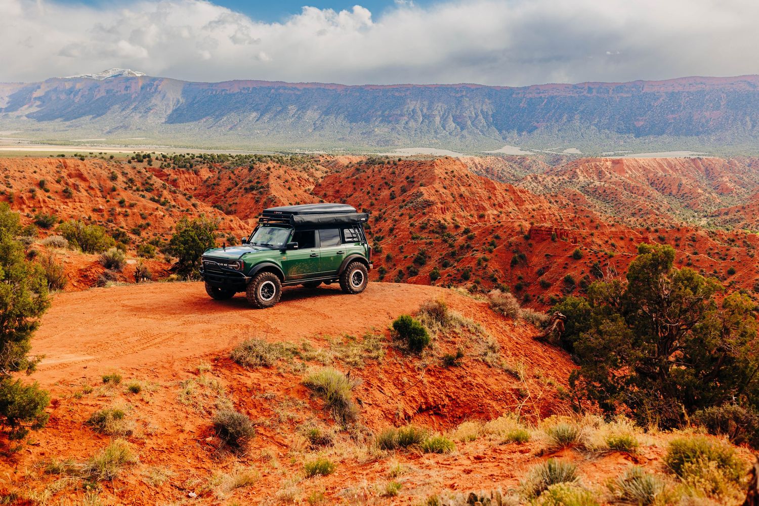 Panoramic desert landscape with red rocks and vehicle in distance.