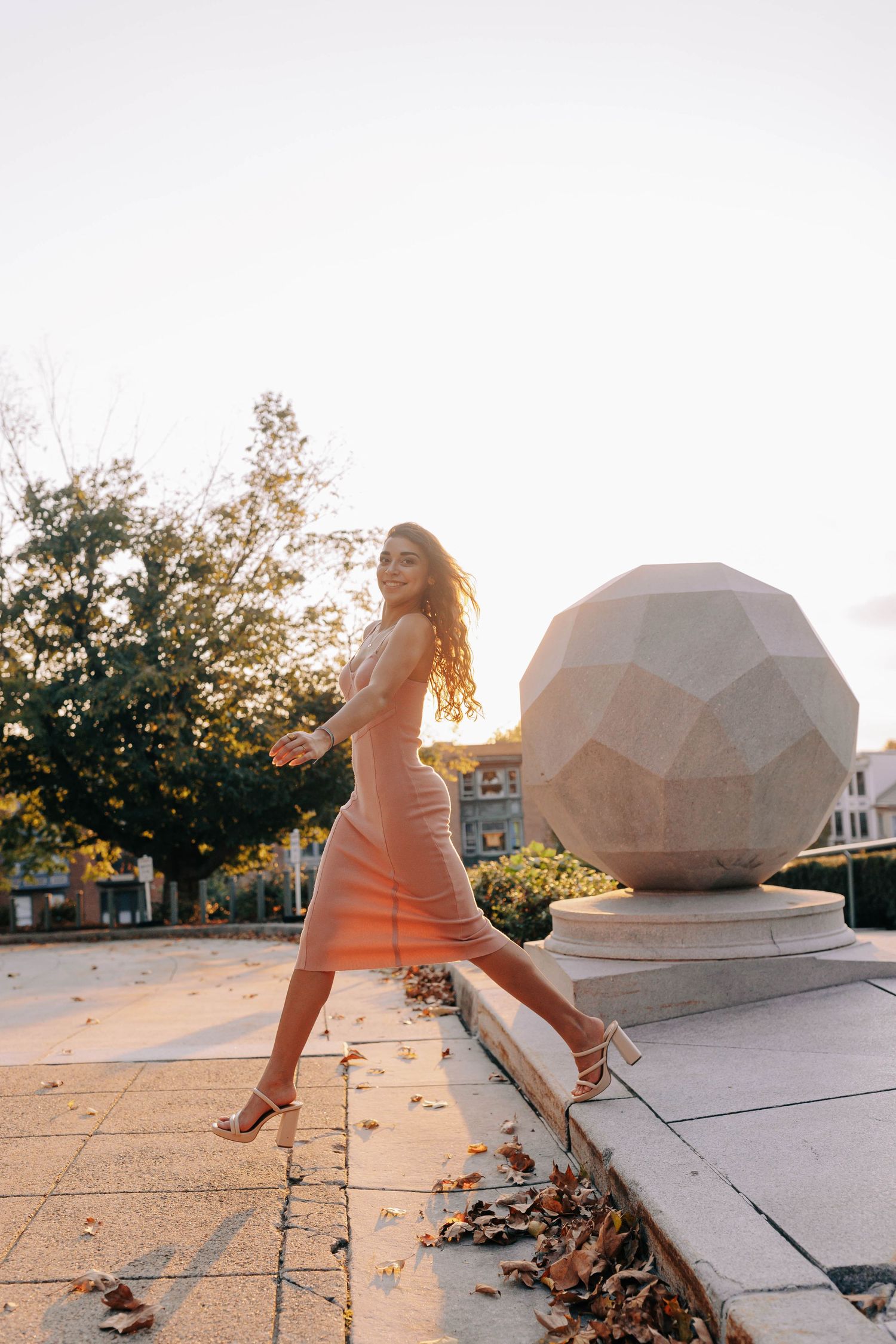 Person in an orange dress poses dramatically at sunset near geometric sculptures.
