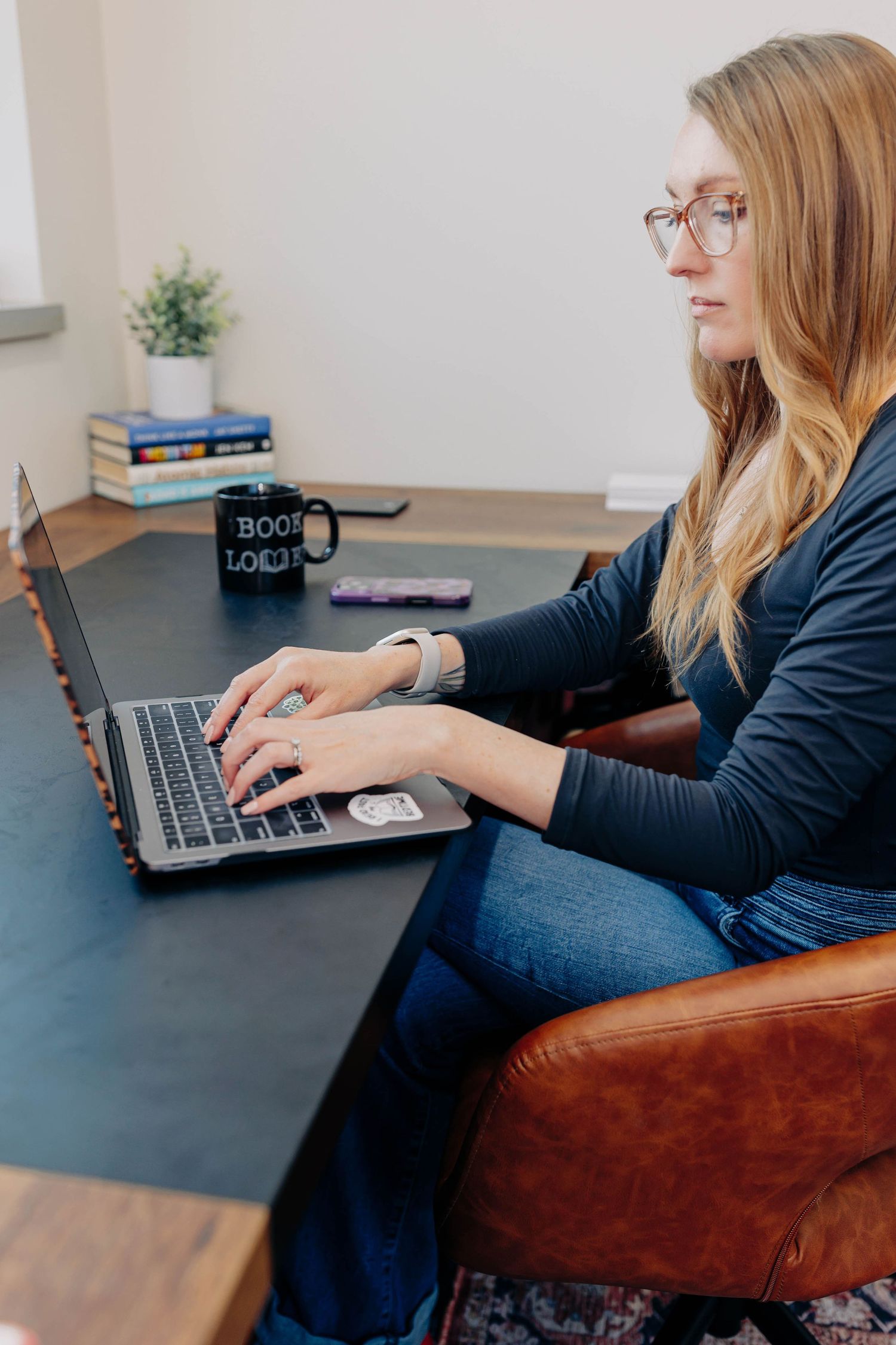 Person working on laptop while seated in brown leather chair at dark desk.