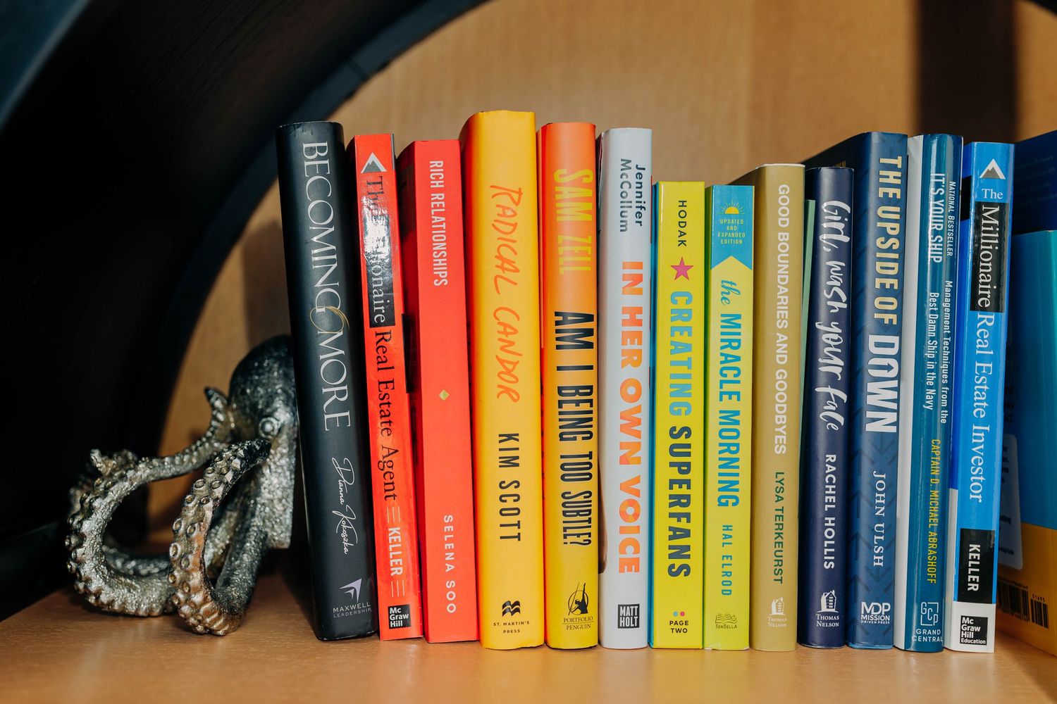 Colorful book spines arranged on a wooden shelf with jewelry accessories.