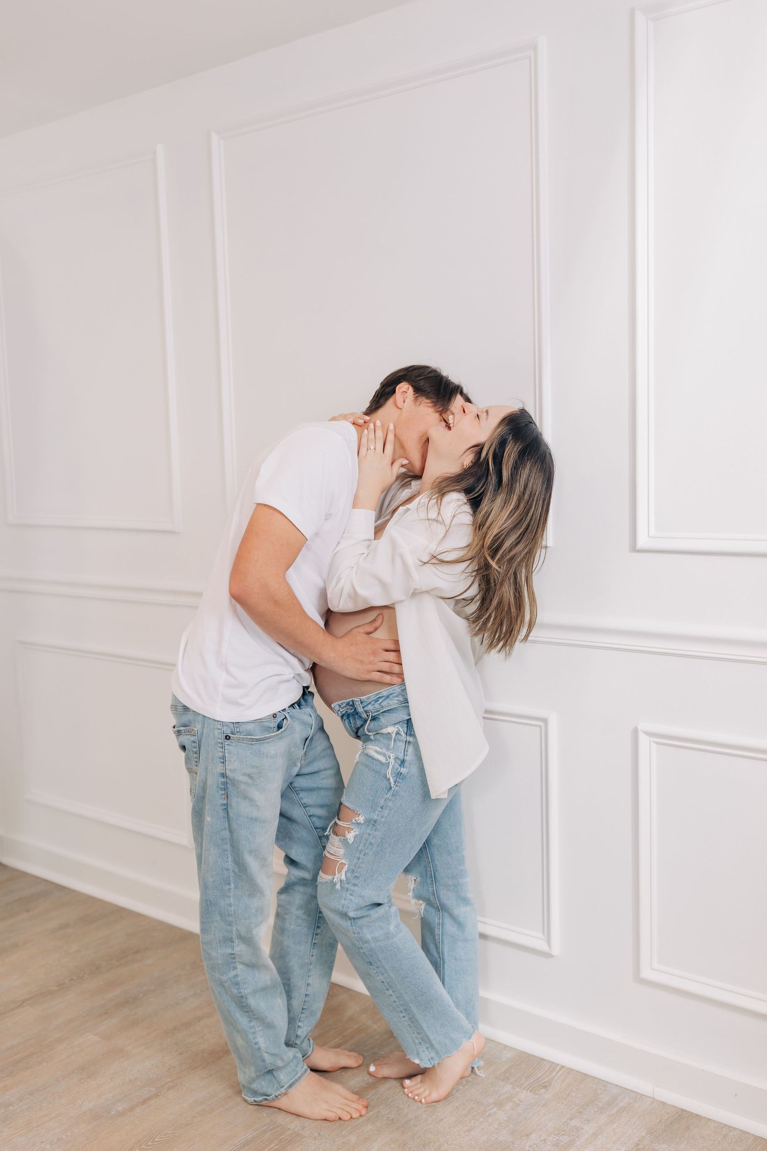 Playful family moment with casual denim and white outfits against white wall.