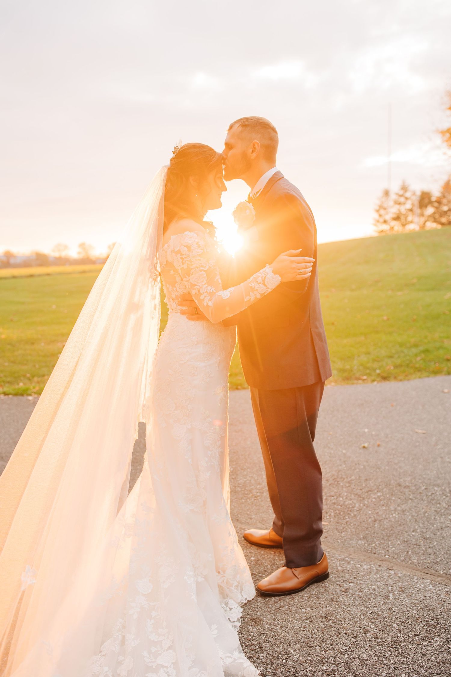 Newlyweds share tender moments in golden sunset light on an outdoor pathway.