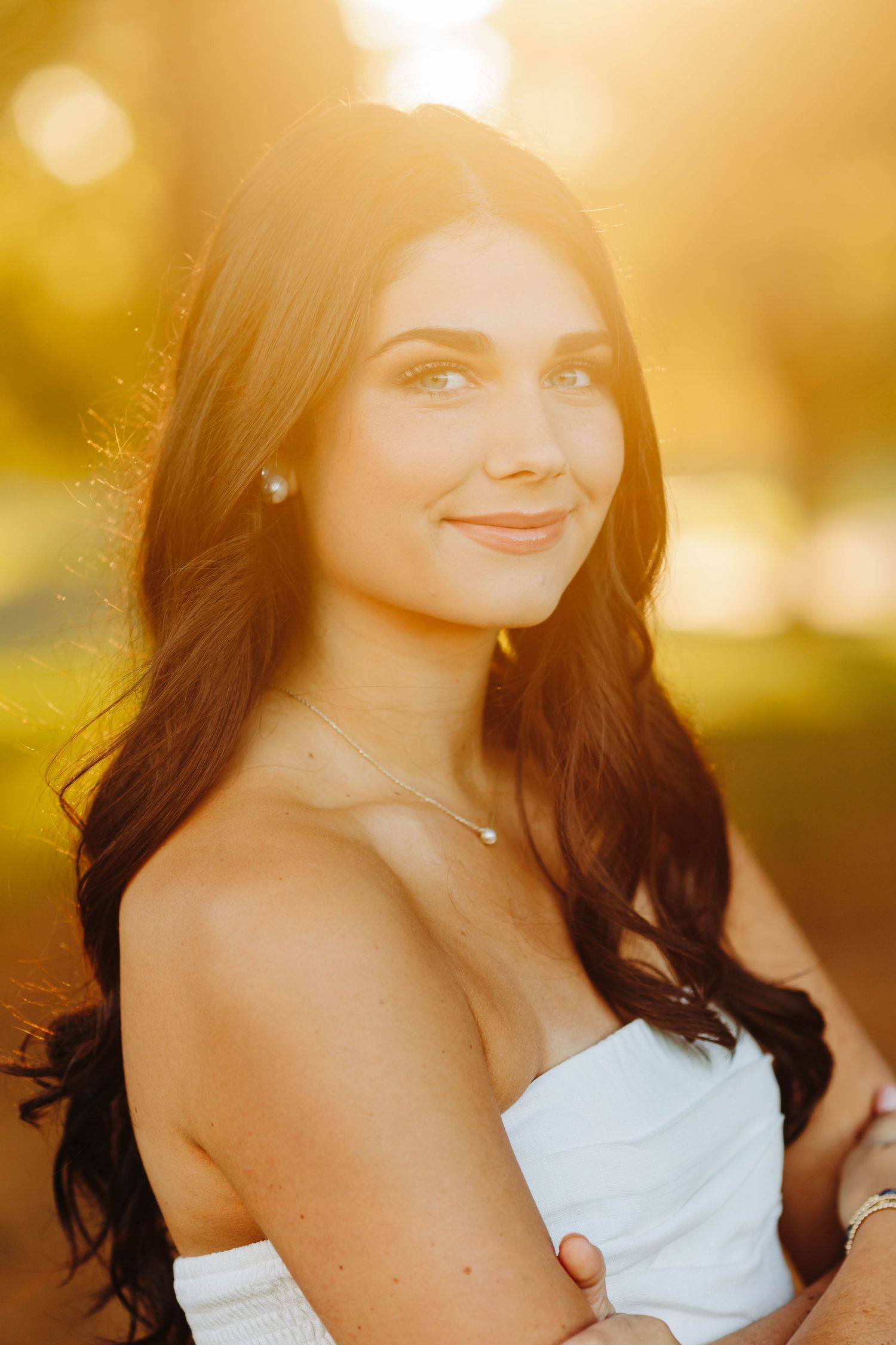 Woman in white dress smiling during golden hour portrait session.