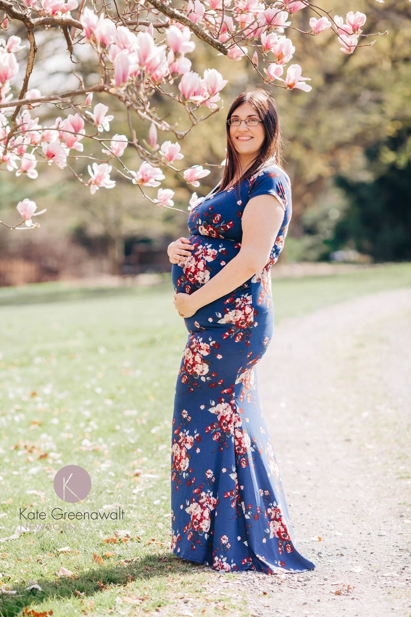 A floral maternity dress photo taken under blooming pink magnolia trees in springtime.