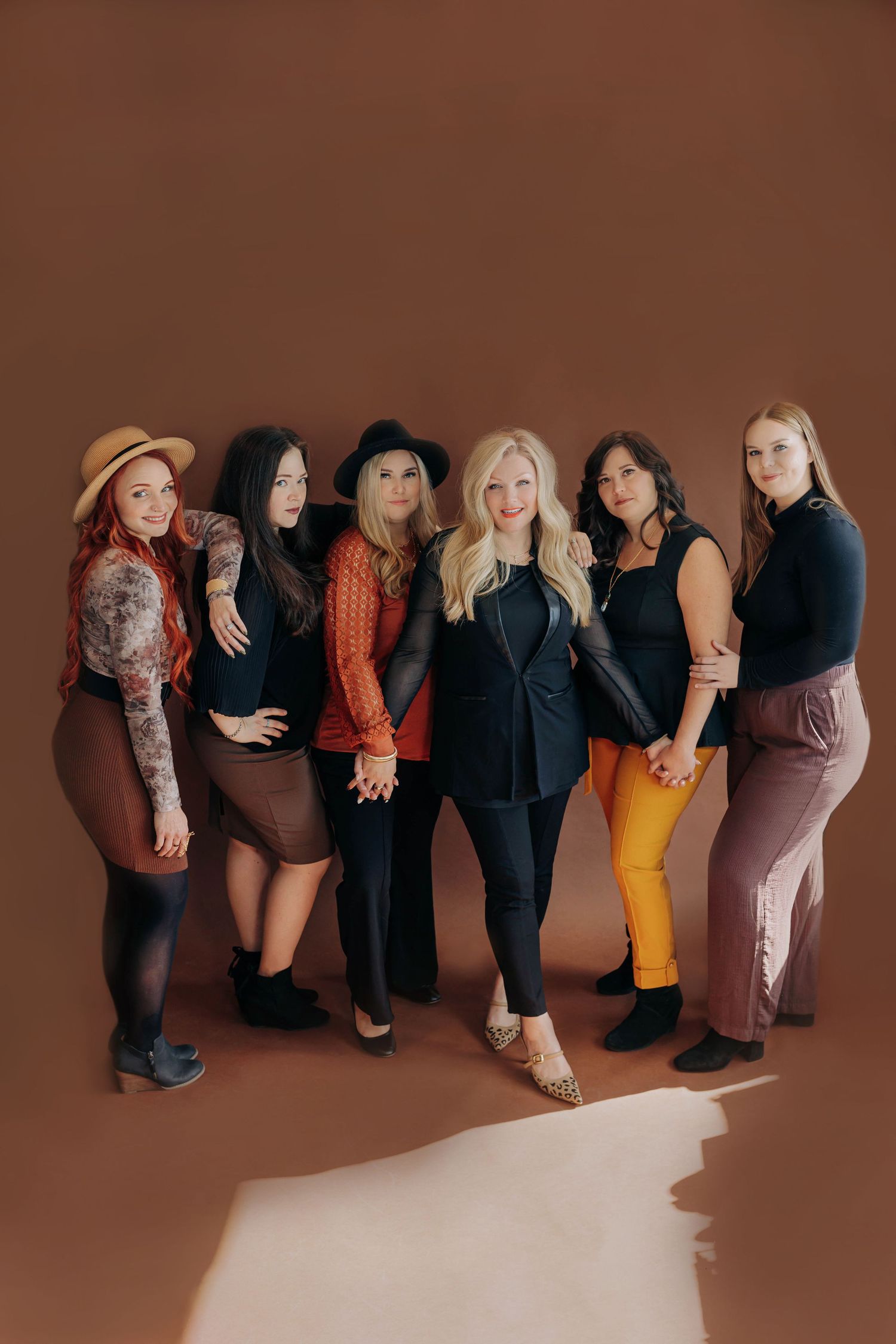 Group fashion photo of women in dark clothing against brown backdrop.