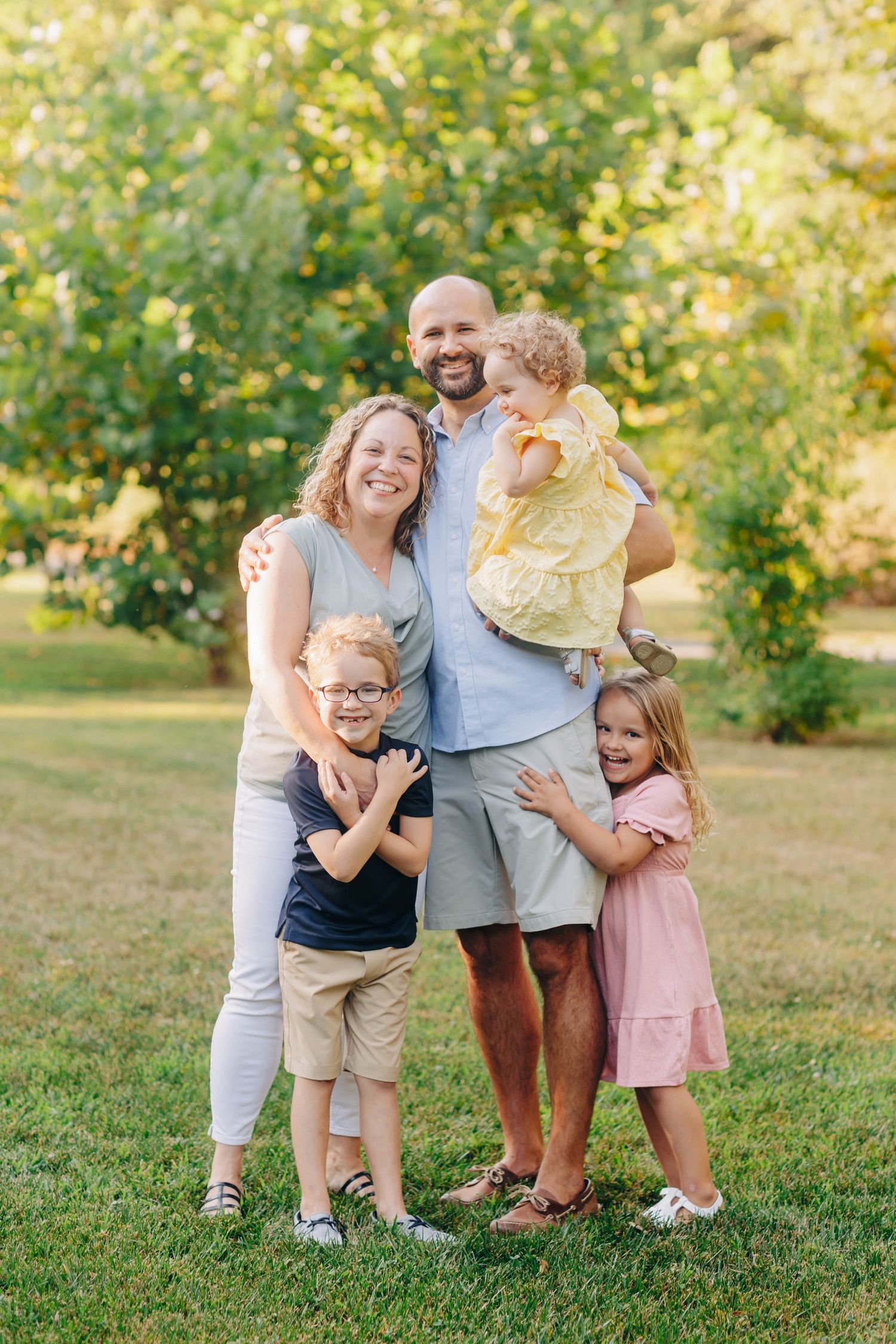 Playful family portrait session on grassy field with natural background.