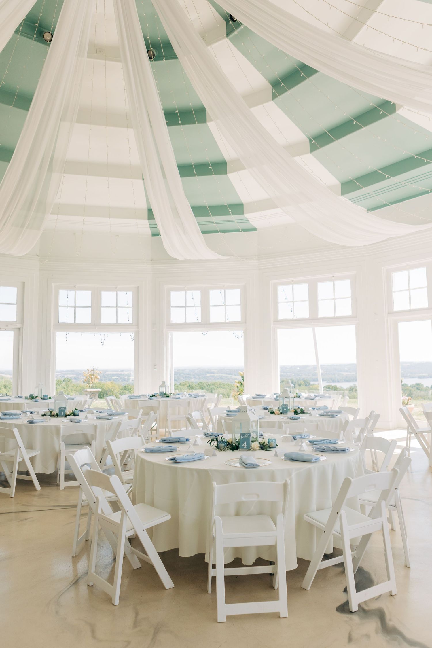 Elegant white wedding reception venue with draped fabric ceiling and round tables set for dinner.