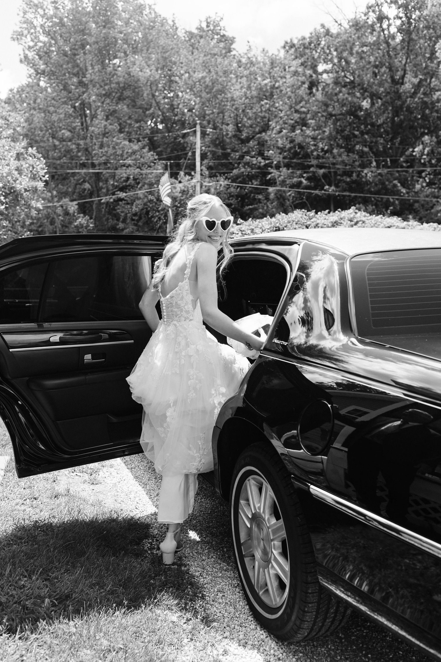 A bride in a flowing white dress entering a luxury black car.