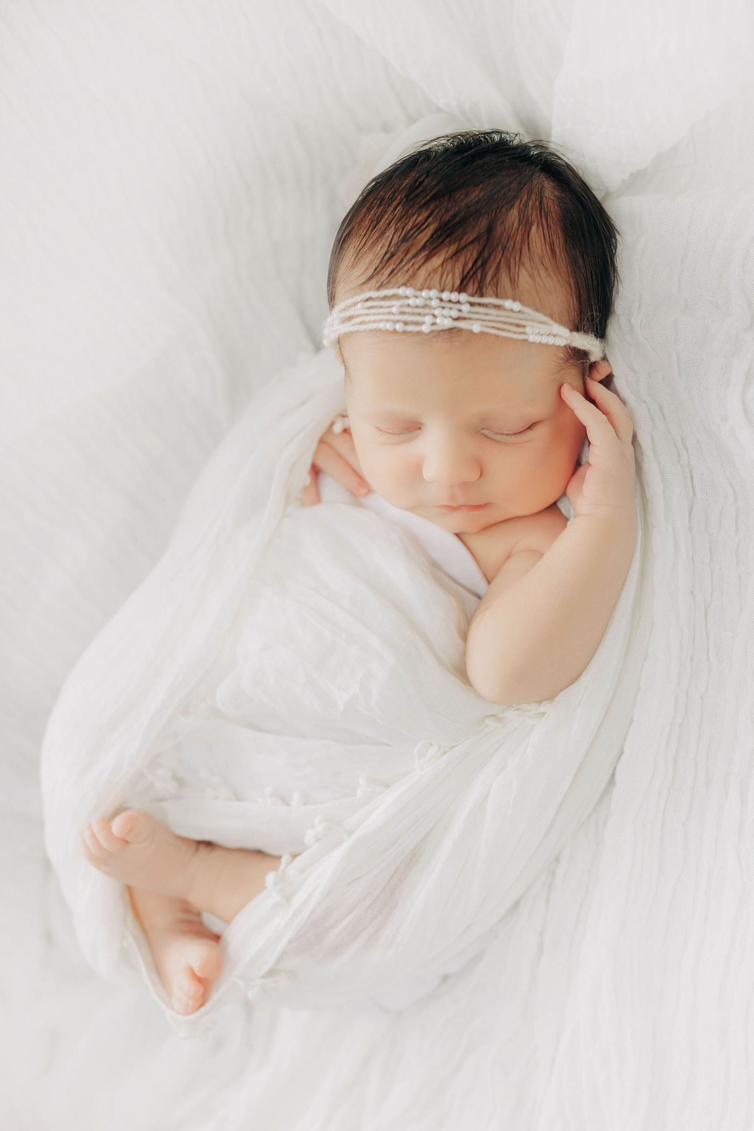 Sleeping newborn baby wrapped in soft white fabric against white background.