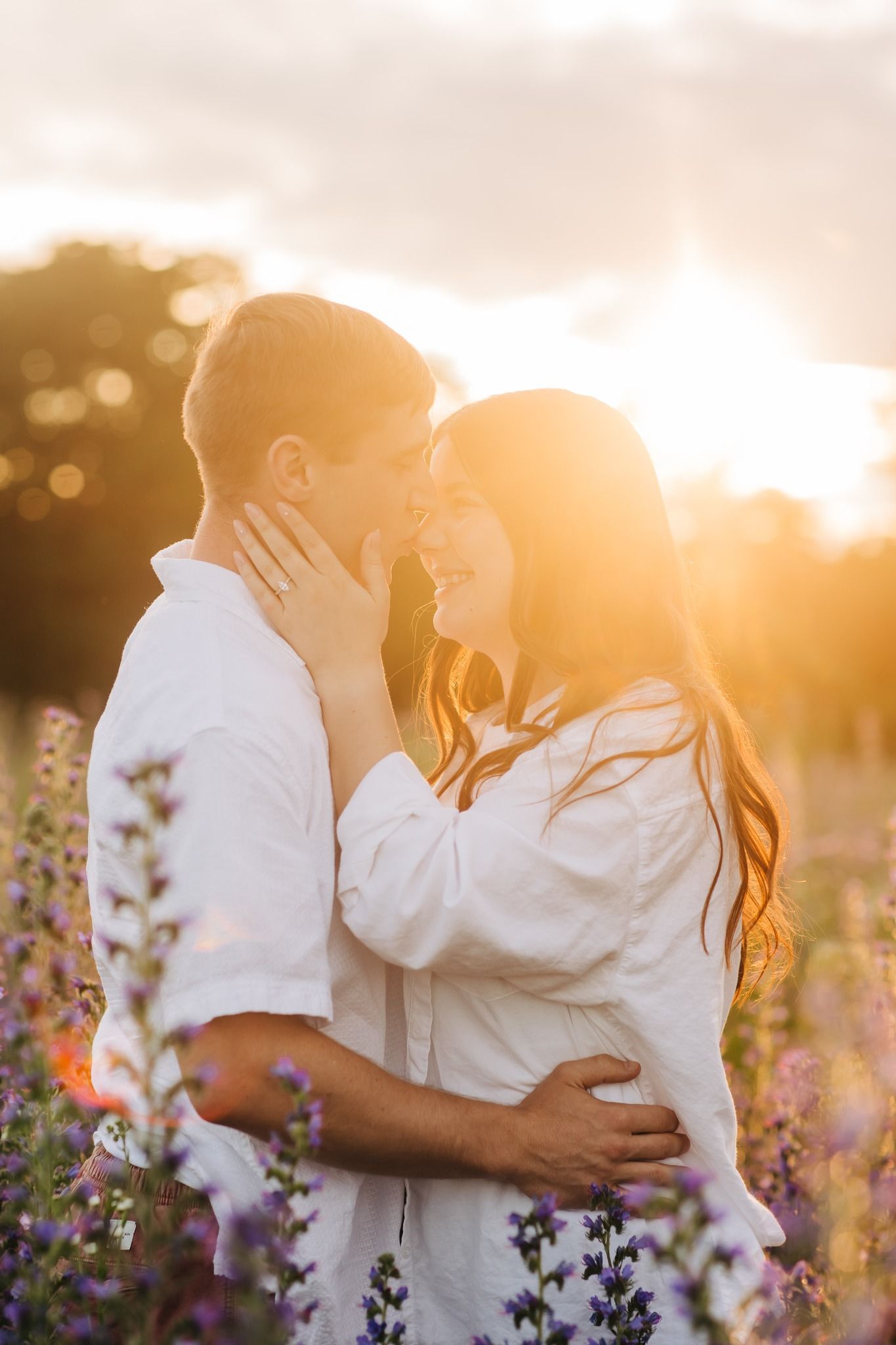 Romantic couple embracing in a field of purple wildflowers at golden hour sunset.
