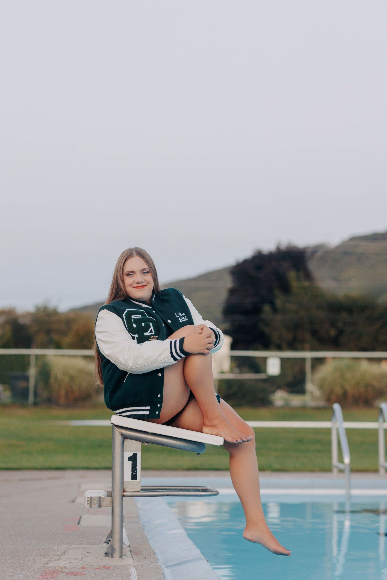 Casual poolside portrait session with varsity jacket and relaxed poses.