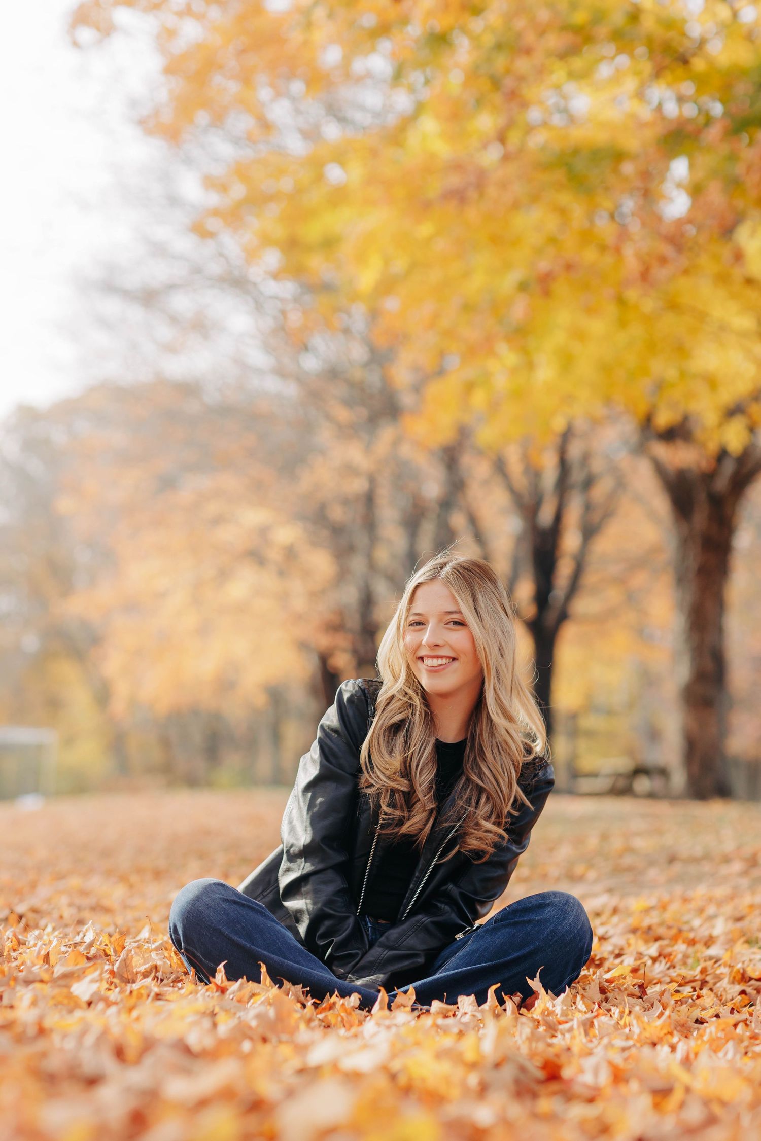 A cozy autumn scene with someone lying in golden fallen leaves wearing a black leather jacket.