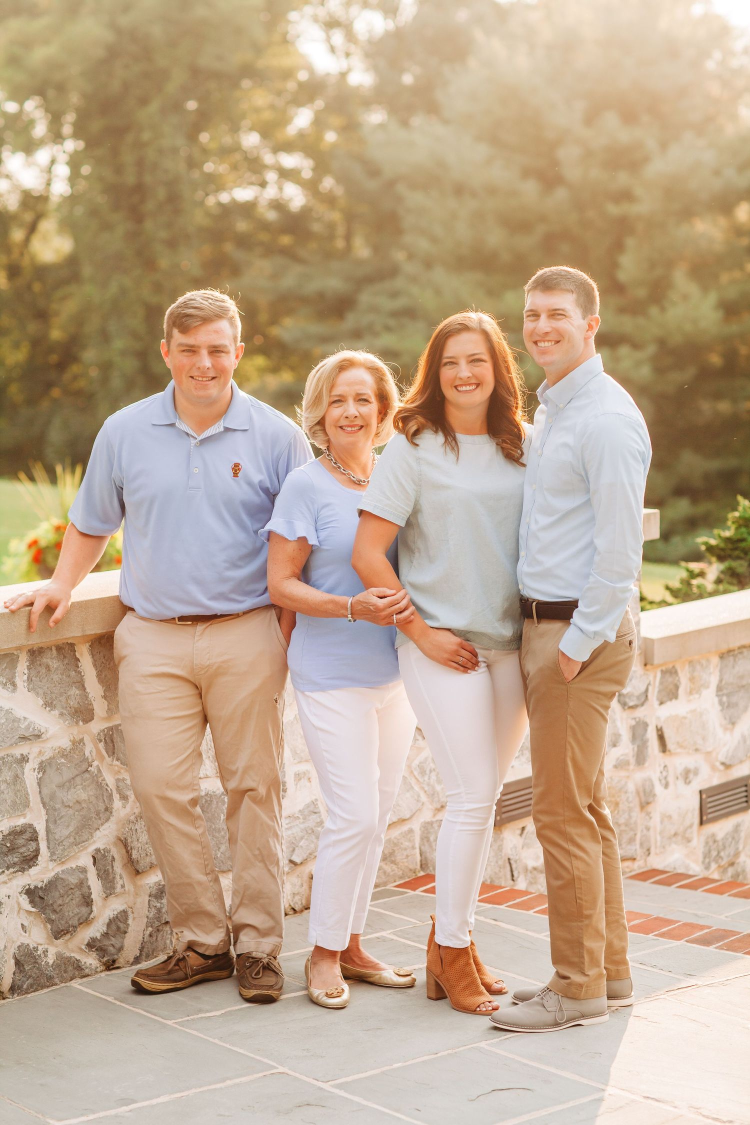 Family group poses together on stone wall during golden hour sunset.
