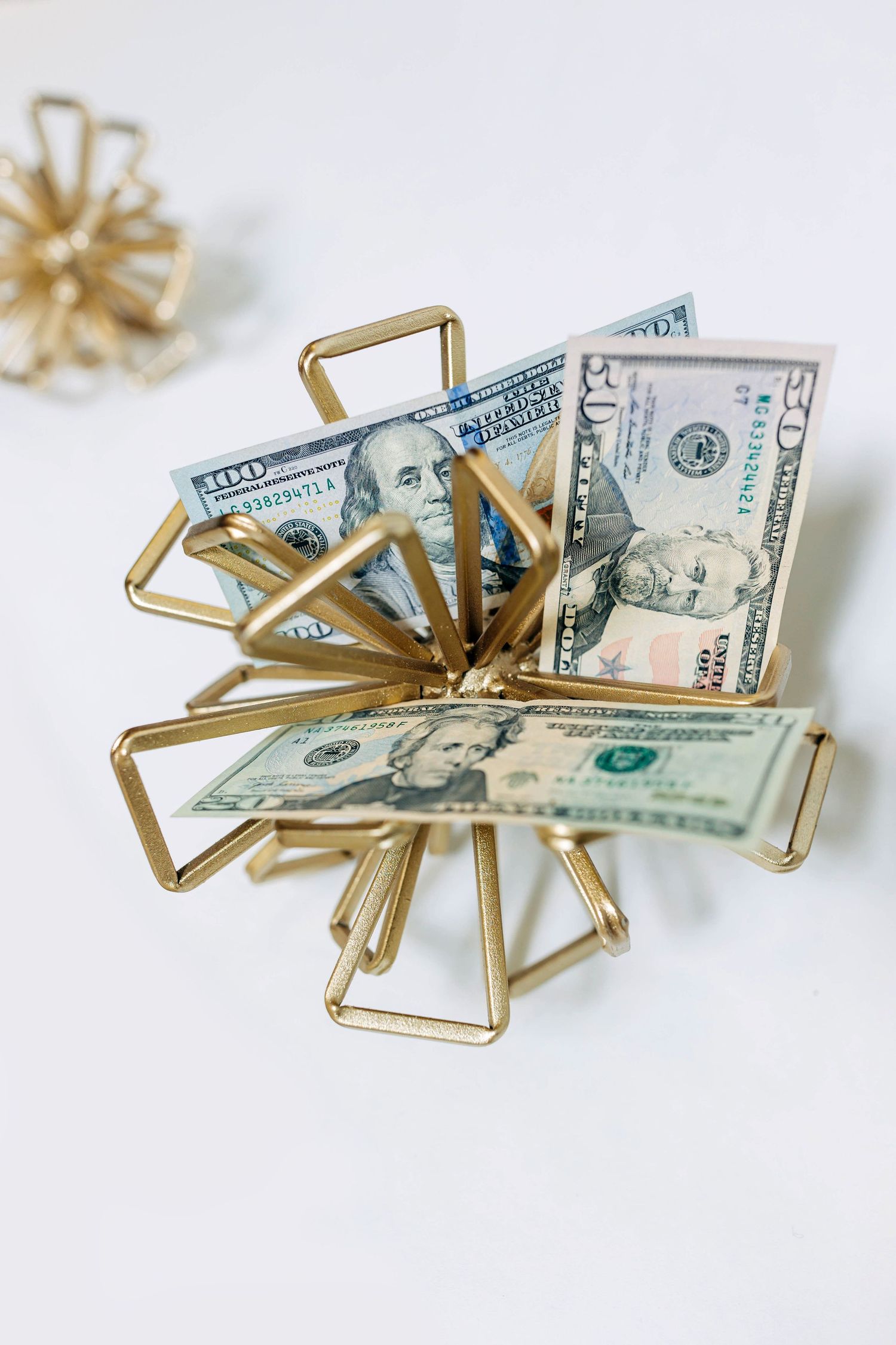 Gold geometric paper clip holder displayed with cash on white background.
