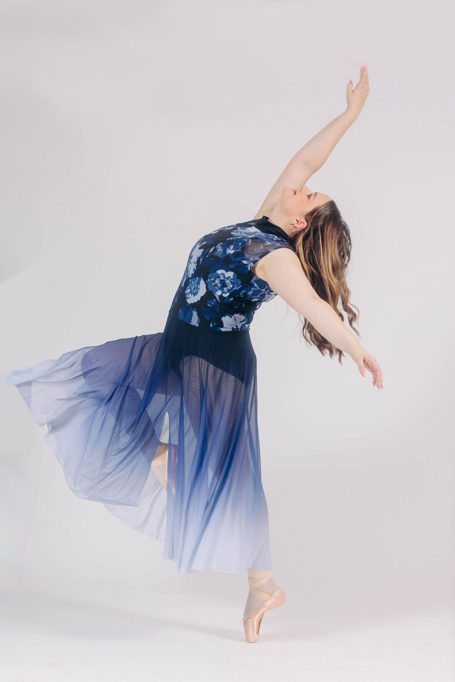 Graceful dance poses in flowing blue tulle dress against white backdrop.