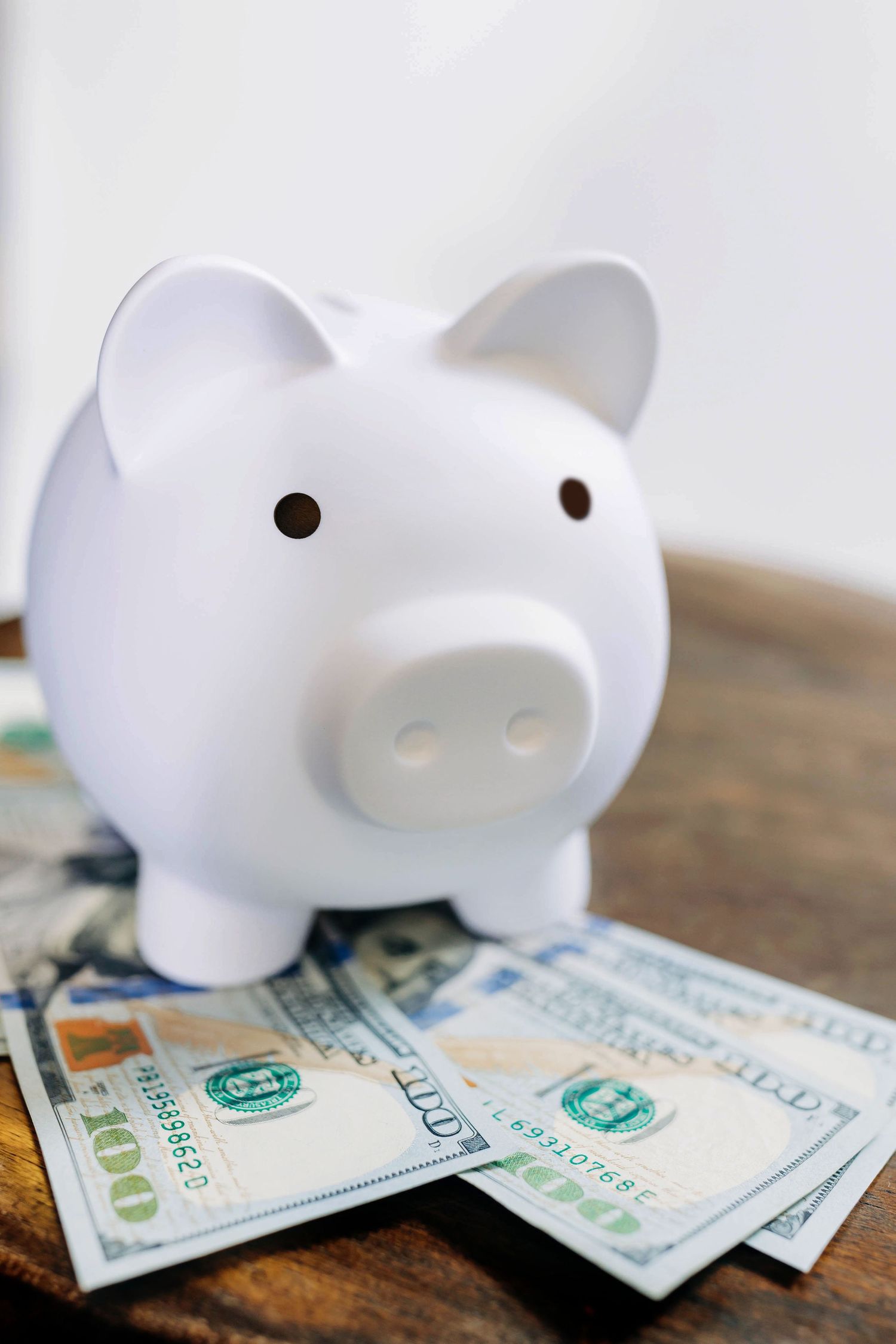 White ceramic piggy bank sitting on spread of hundred dollar bills.