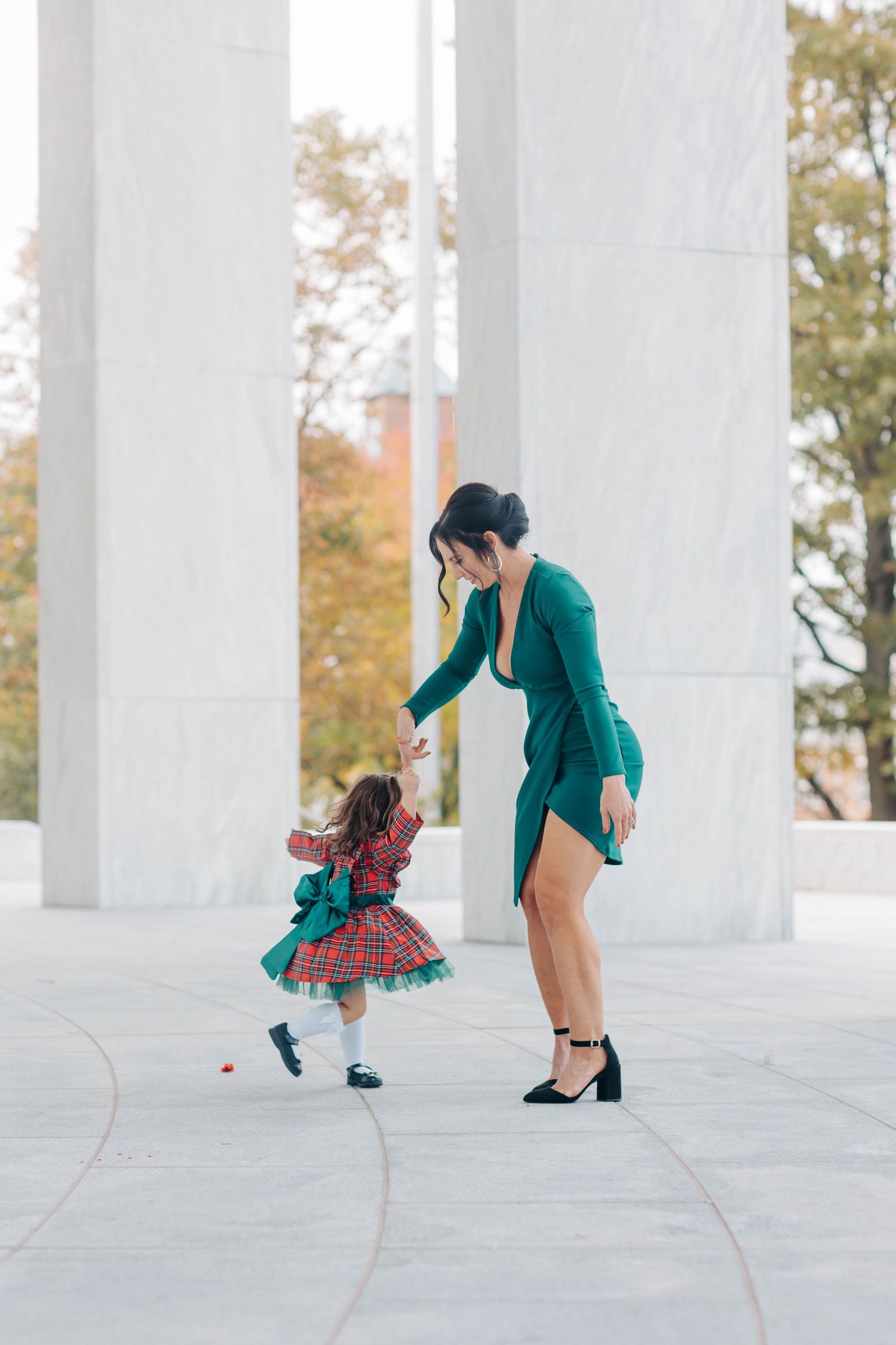Person in green jacket and plaid skirt jumping playfully between white columns.