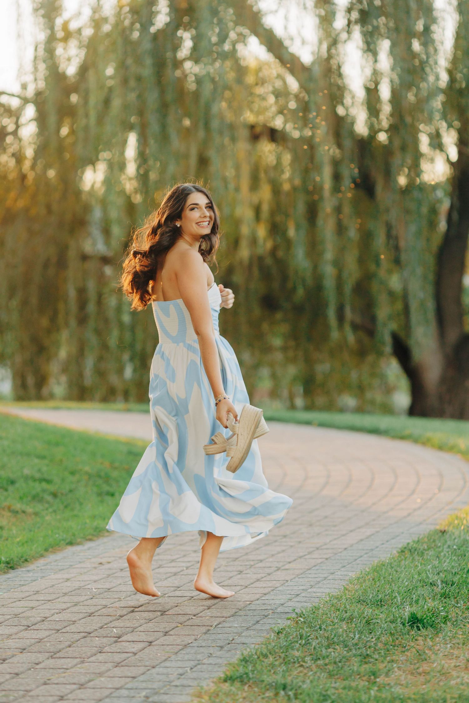 Dancing in a light blue dress along a garden path at sunset.