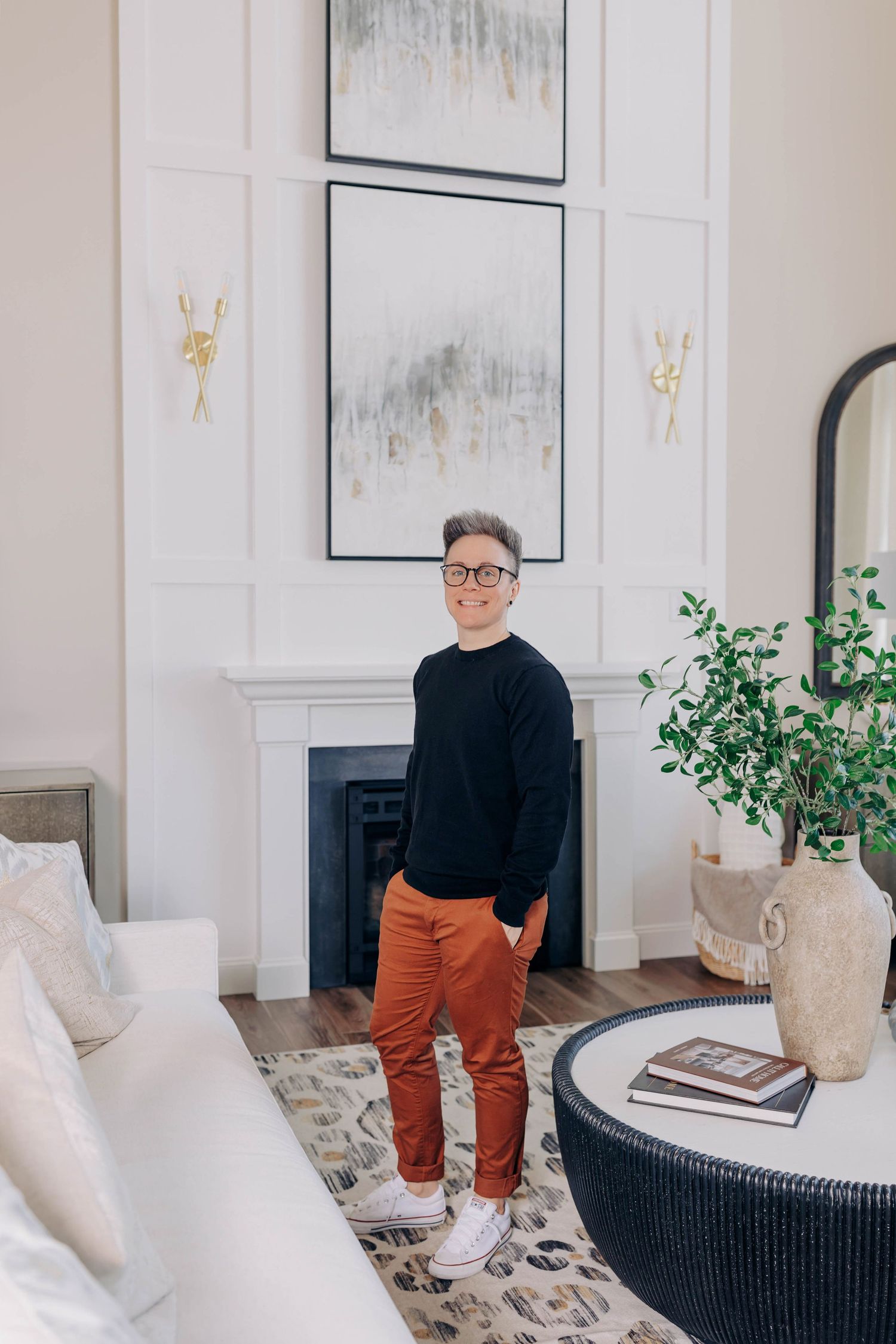 A cozy living room interior features black wicker chairs, orange pants, and white artwork on the walls.
